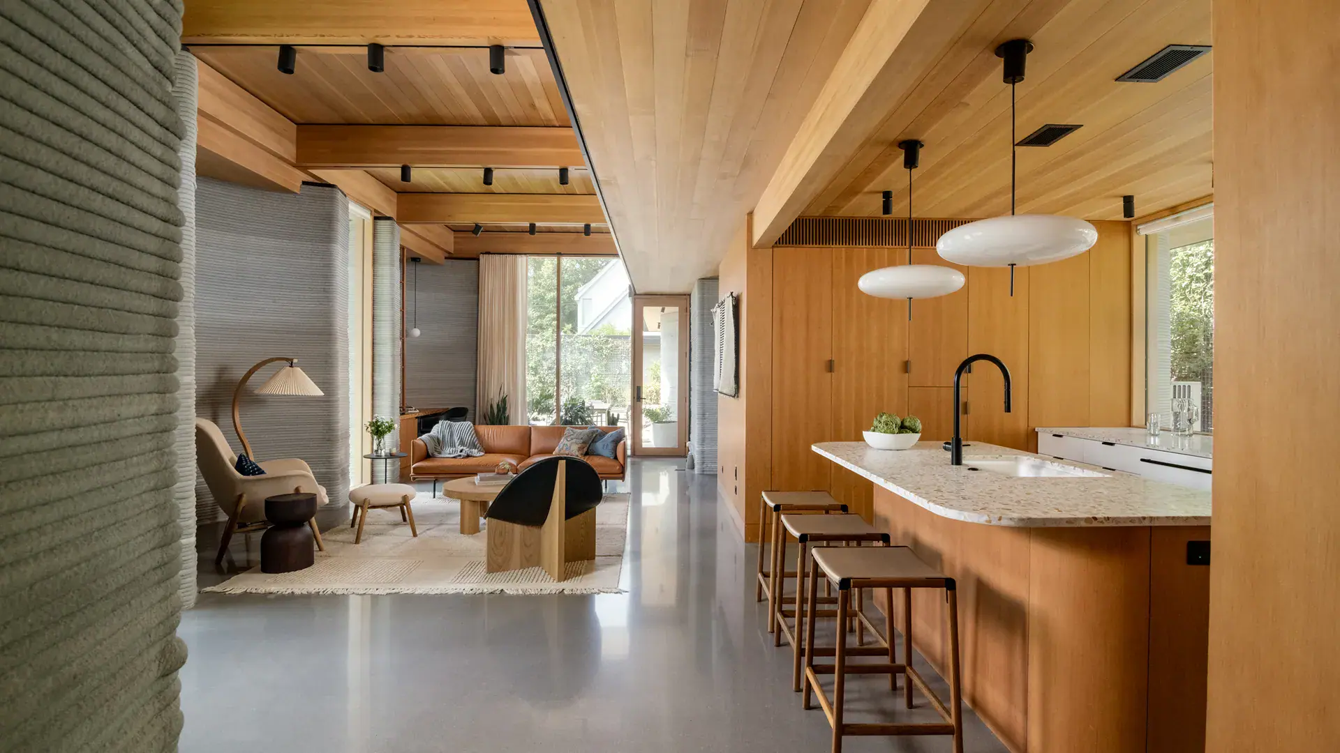 Open-plan living room and kitchen with wood ceiling, terrazzo island, leather sofa and bar stools