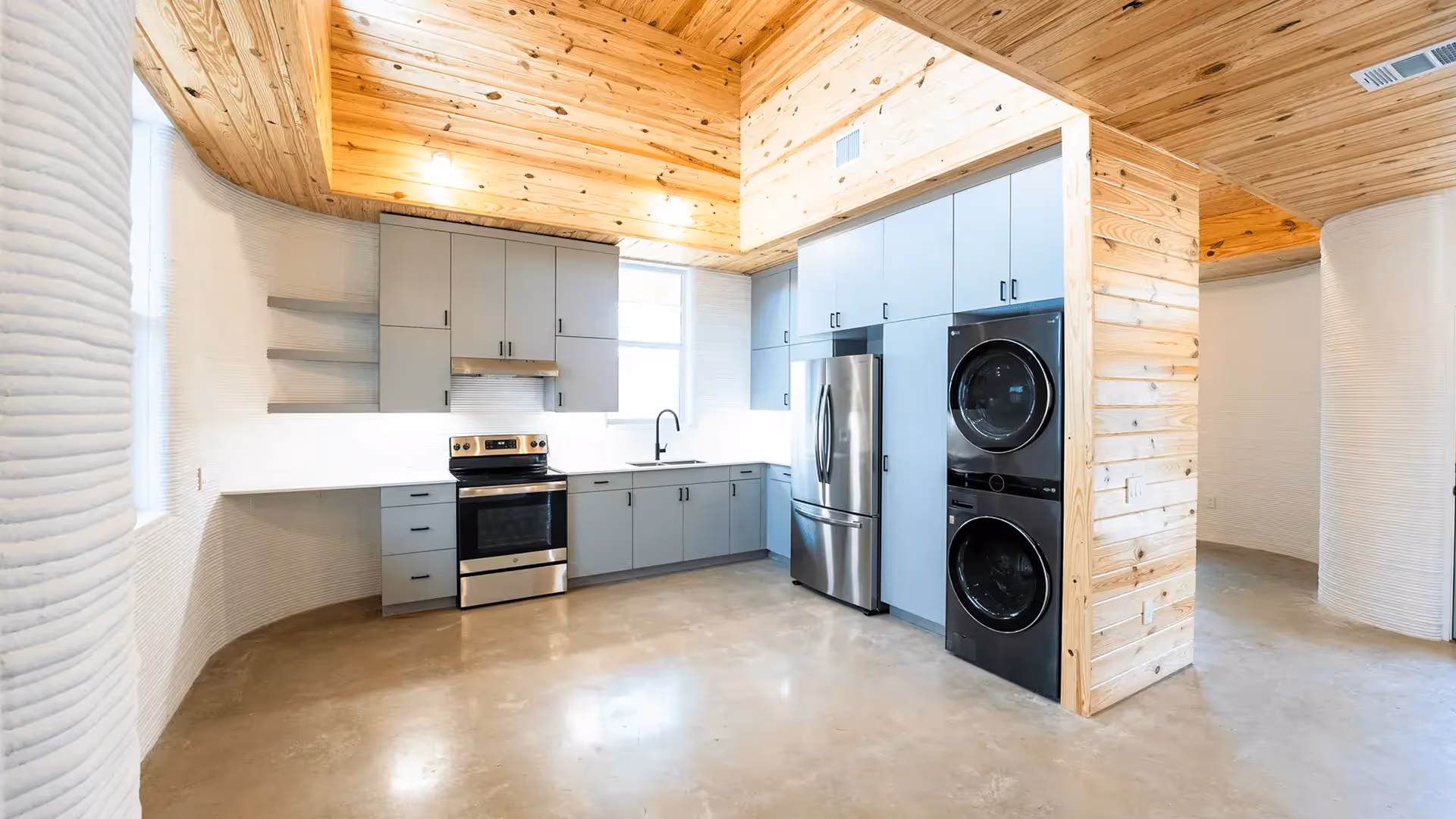 Kitchen with gray cabinets, stainless steel stove and fridge, stacked washer-dryer and wood ceiling