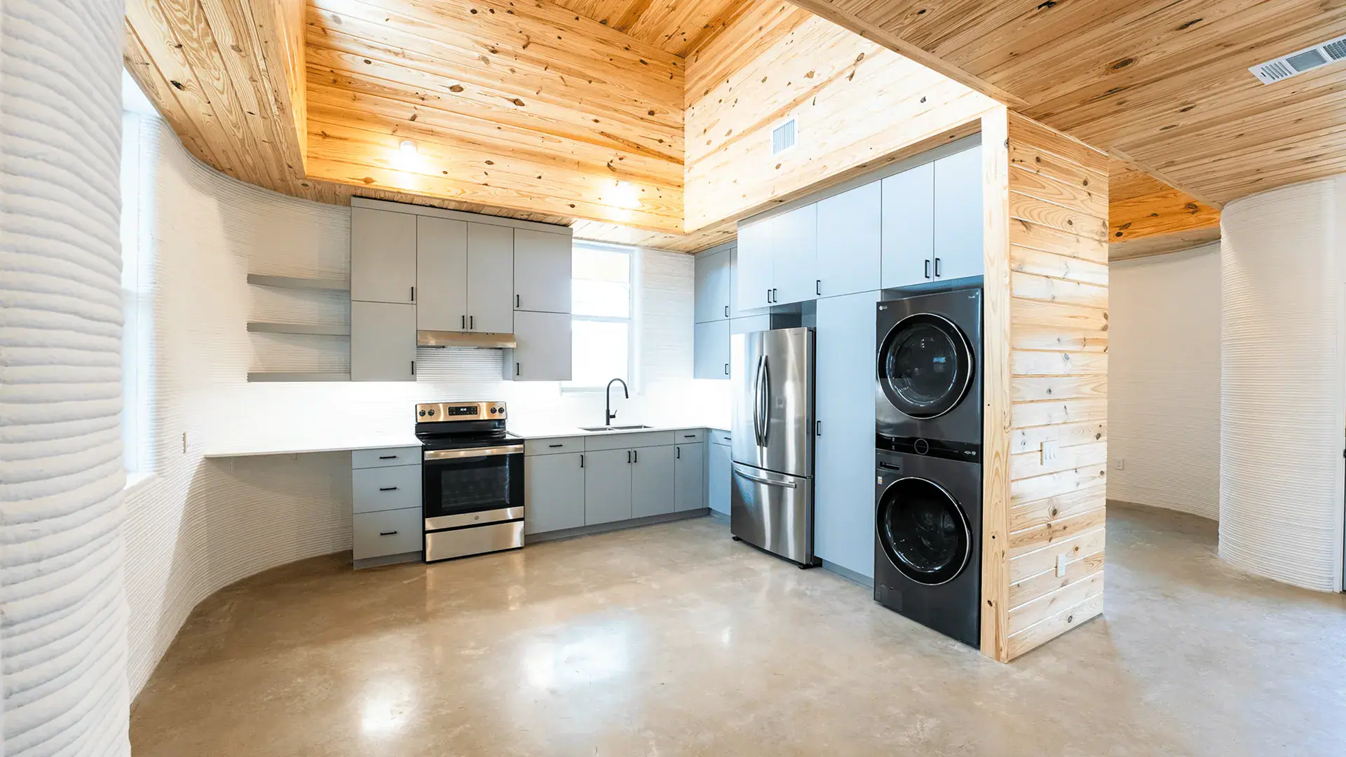 Kitchen with gray cabinets, stainless steel stove and fridge, stacked washer-dryer and wood ceiling