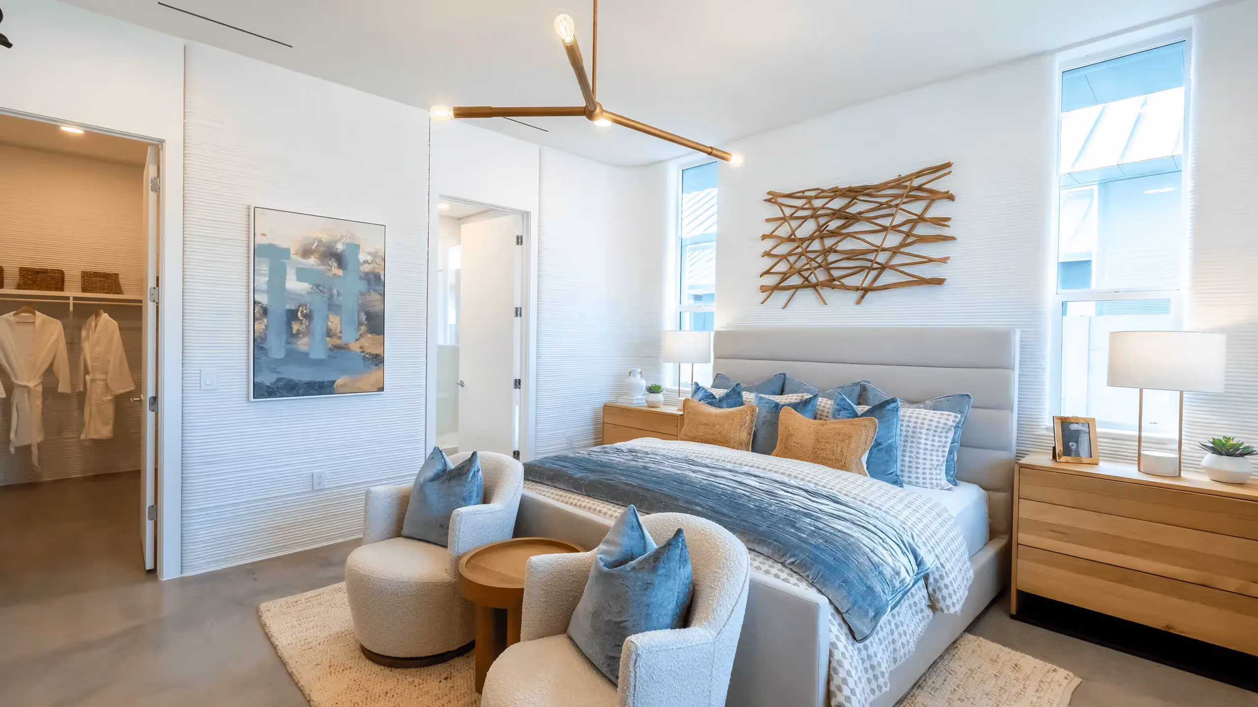 Modern bedroom with upholstered bed, blue pillows, wooden nightstands, and two armchairs