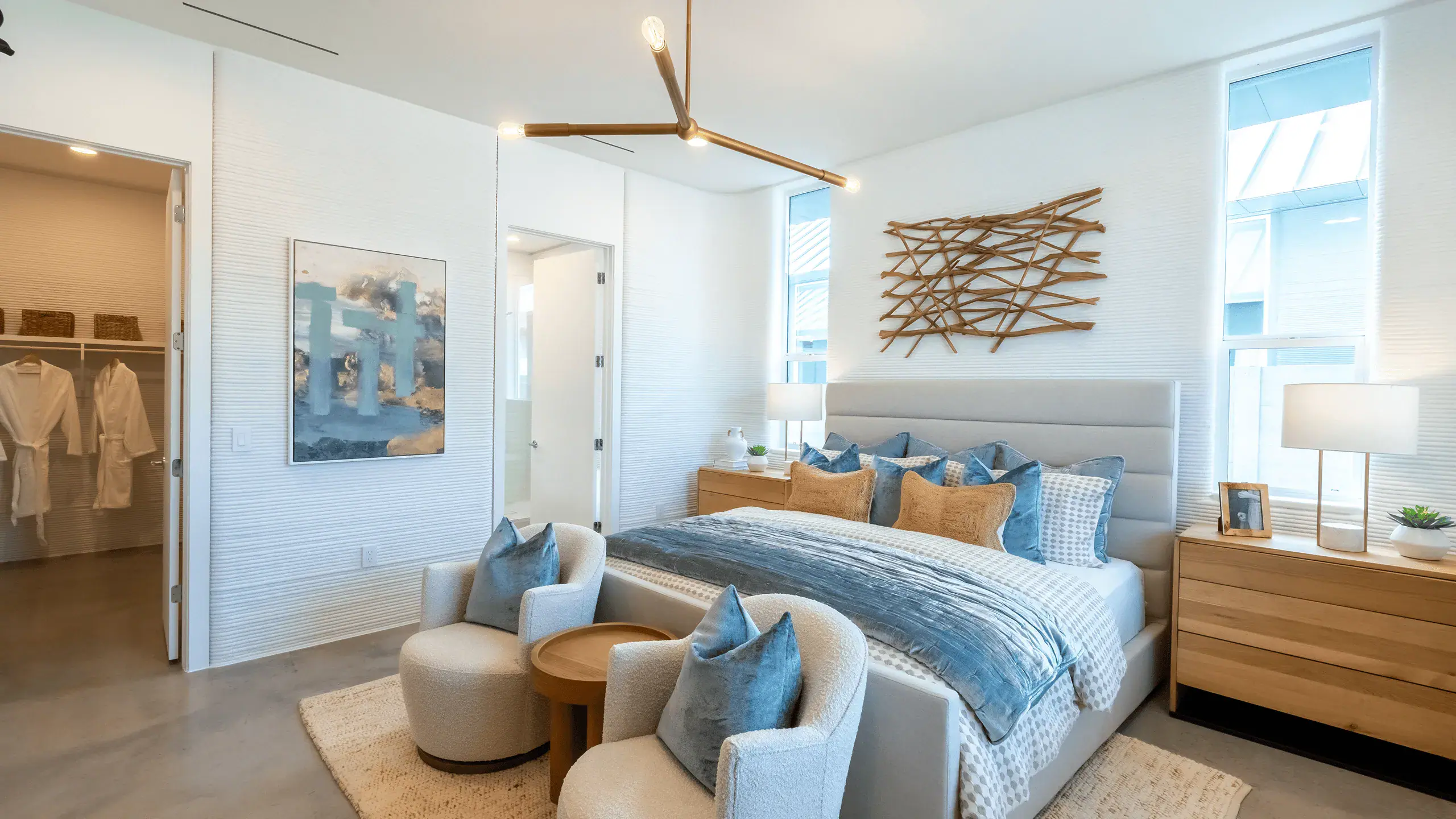 Modern bedroom with upholstered bed, blue pillows, wooden nightstands, and two armchairs