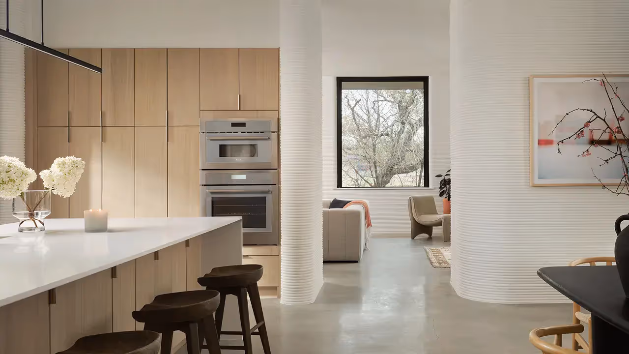 Open-plan kitchen and living area with white island, wood cabinets, stainless double oven, ribbed columns