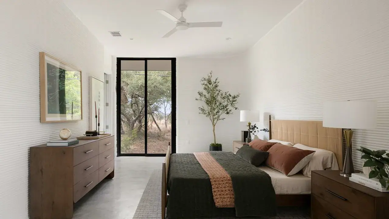 Modern bedroom with wooden bed and dressers, lamps, ceiling fan, and sliding glass door with trees