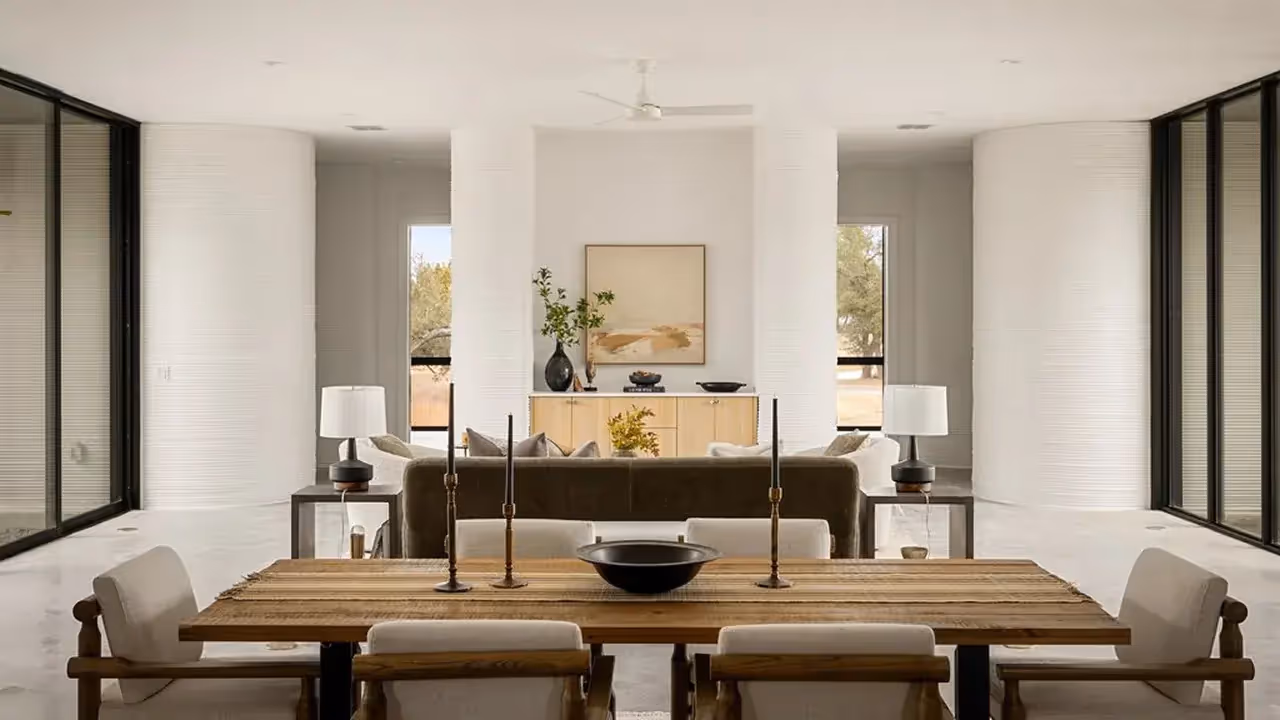 Open living and dining room with wooden table, candlesticks, sofa, console, and layered white curved walls