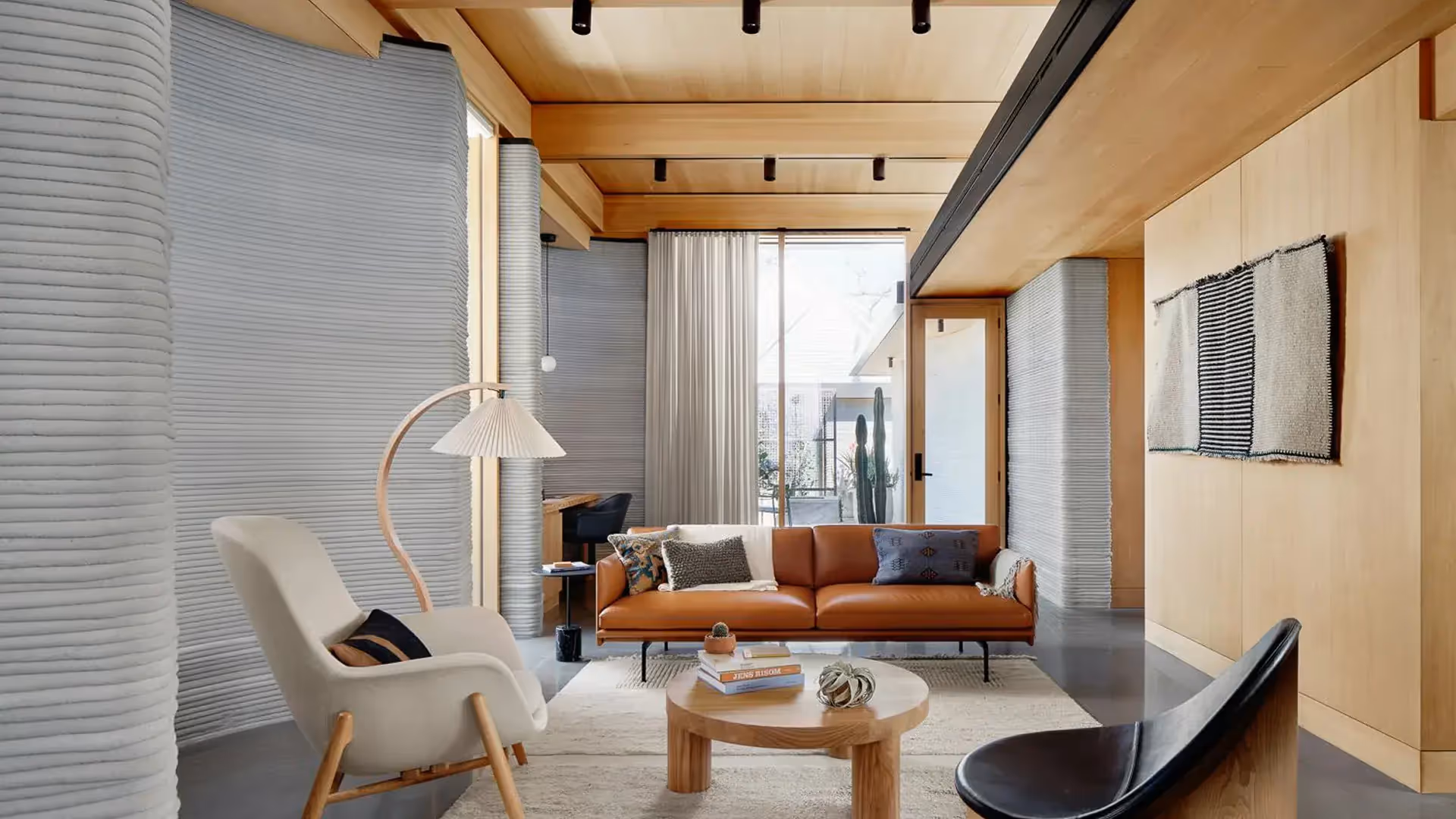 Modern living room with tan leather sofa, wooden coffee table, armchairs, floor lamp, and ribbed walls