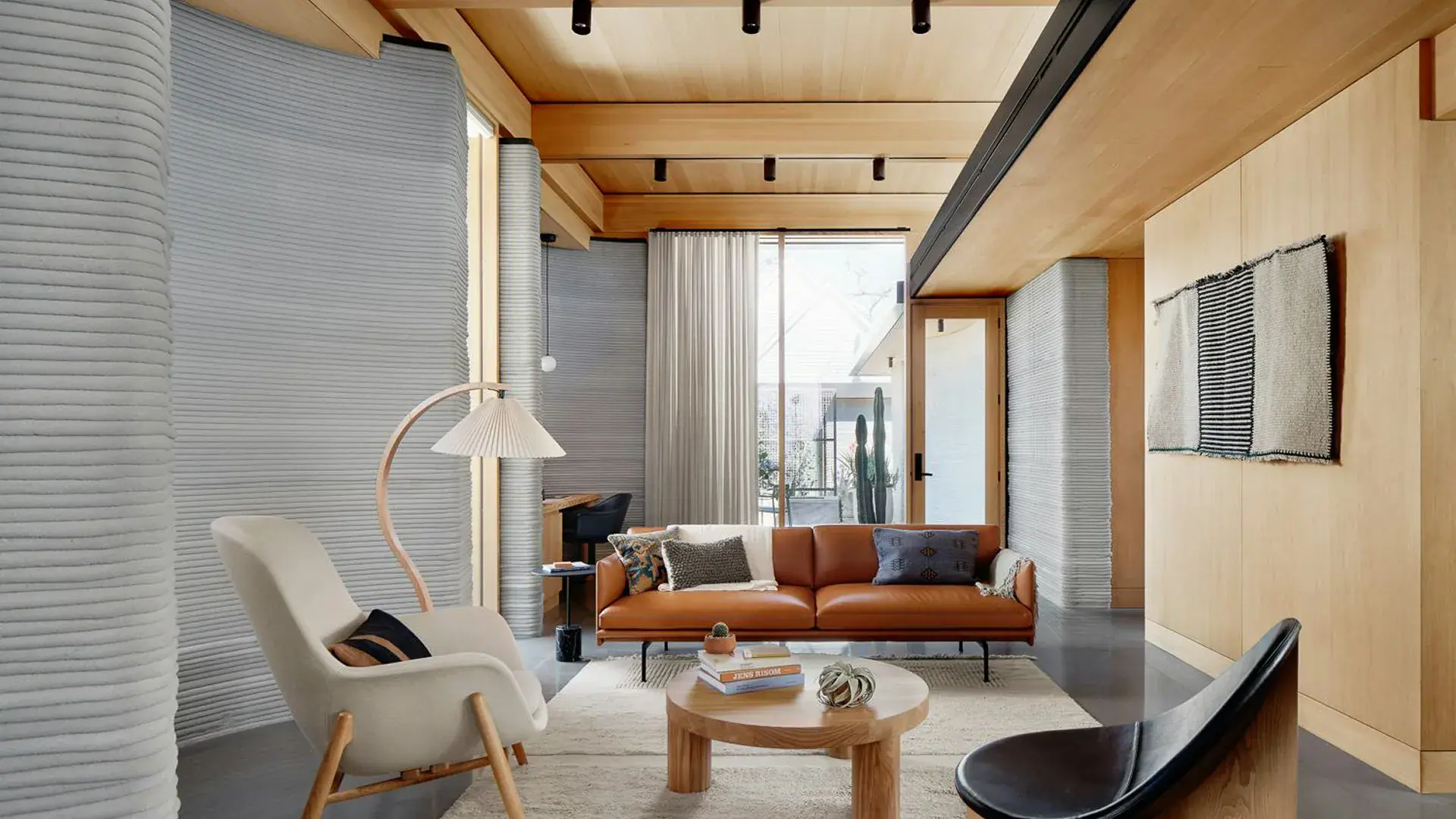 Modern living room with tan leather sofa, wooden coffee table, armchairs, floor lamp, and ribbed walls
