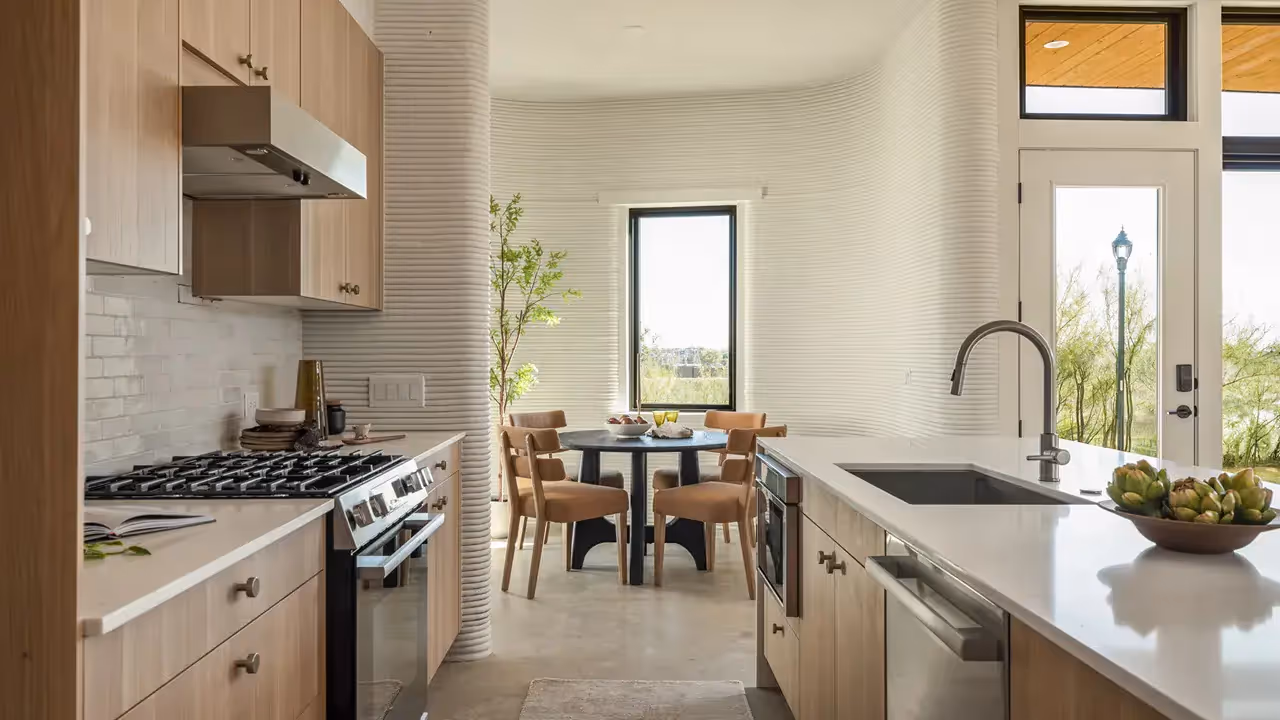 Modern kitchen with wood cabinets, island sink, gas range, round dining table and ribbed curved wall