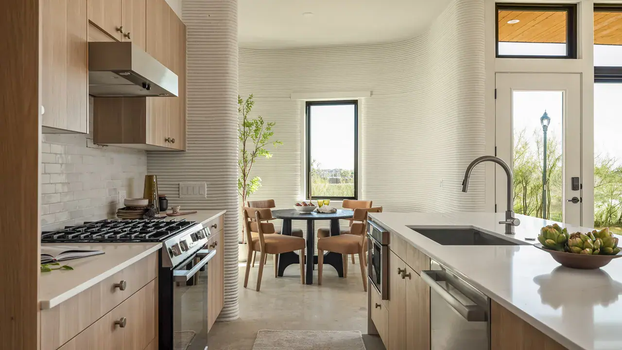 Modern kitchen with wood cabinets, island sink, gas range, round dining table and ribbed curved wall