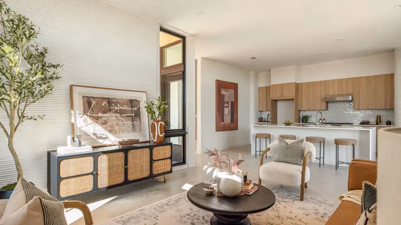 Open-plan living room and kitchen with rattan console, round coffee table, and kitchen island with stools