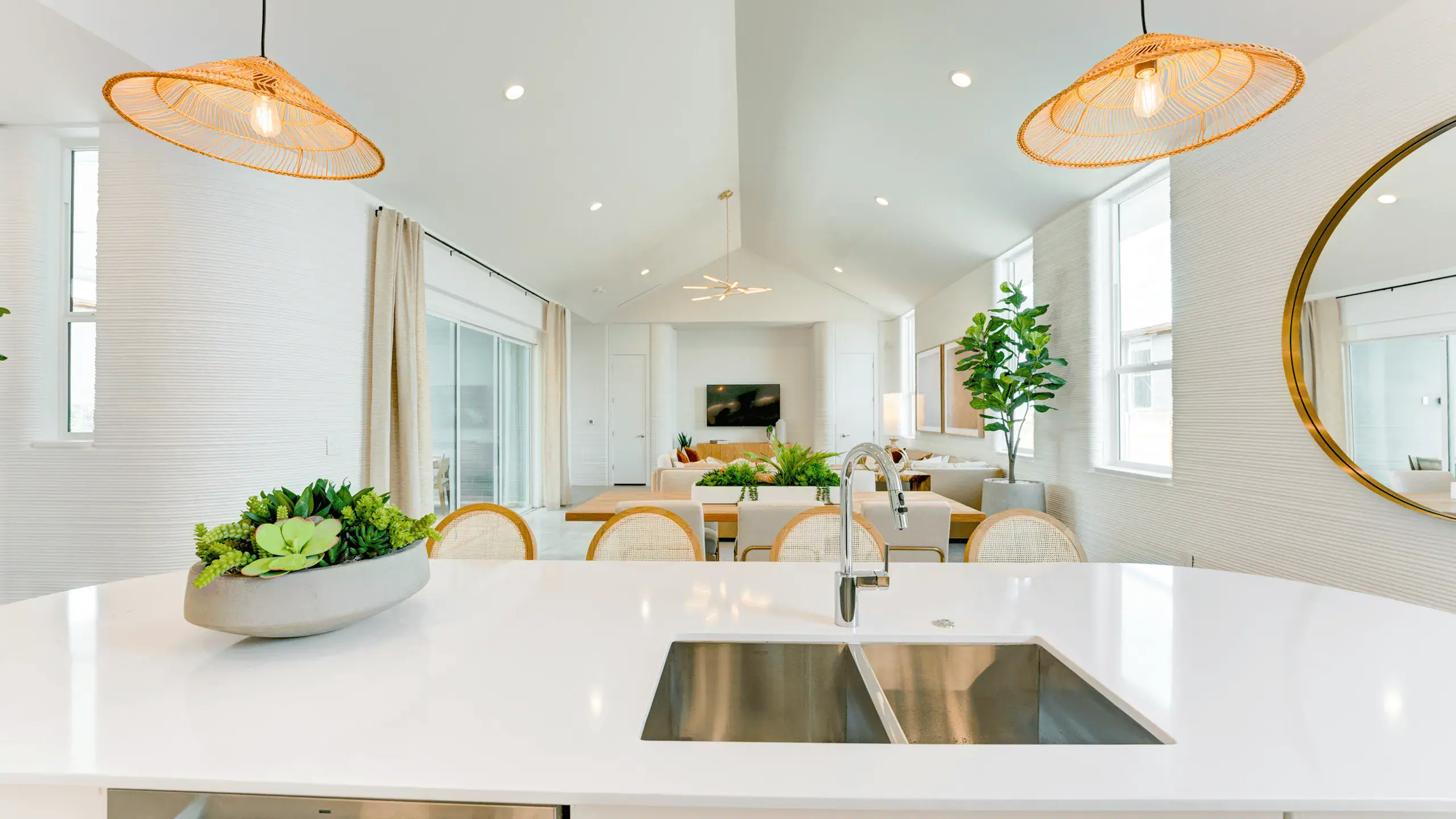 Open-plan kitchen and living area with white island, stainless sink, pendant lights, and plants
