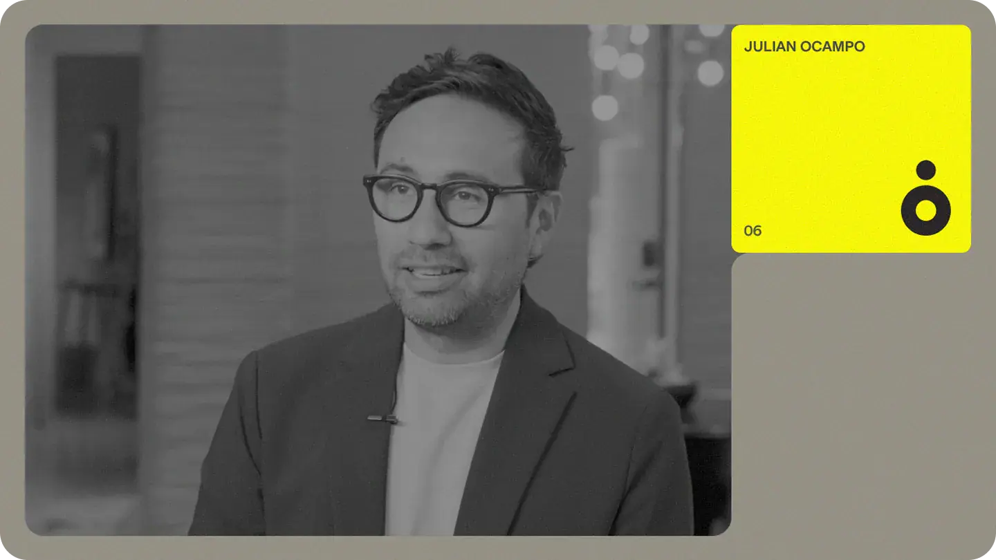 Interview portrait of a team member in glasses and blazer with a bright profile card overlay labeled "Julian Ocampo"
