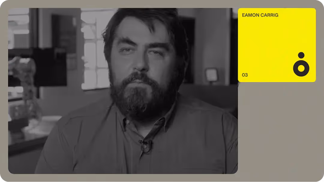 Grayscale headshot of a bearded staff member in an office with blurred robotic arm and yellow profile card overlay