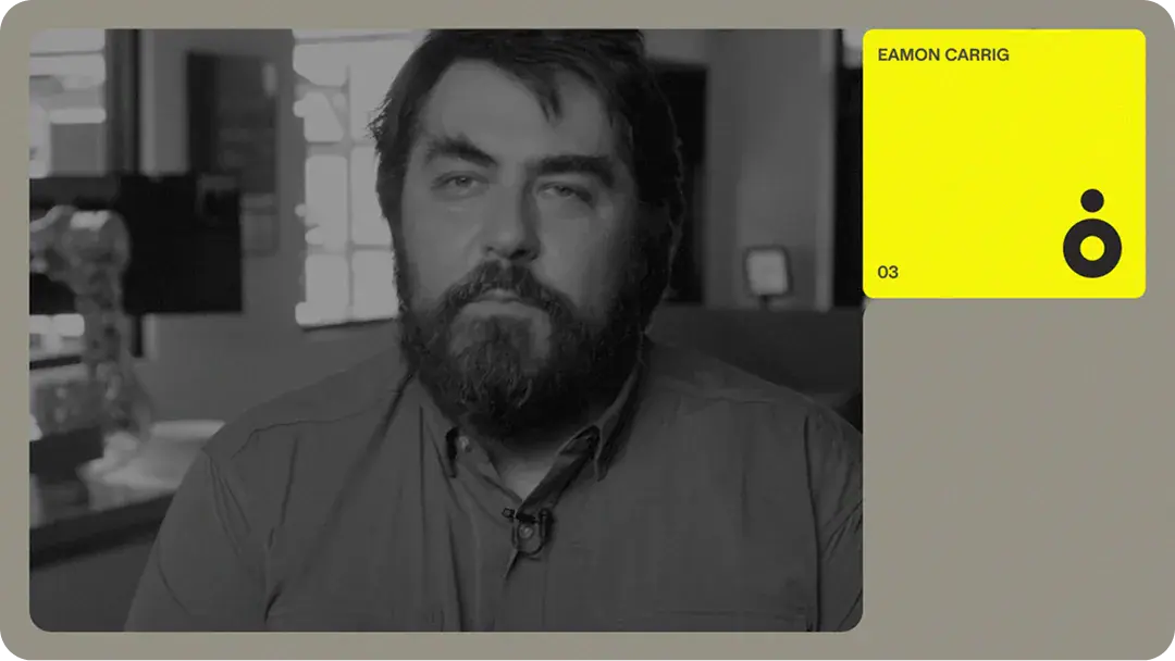 Grayscale headshot of a bearded staff member in an office with blurred robotic arm and yellow profile card overlay