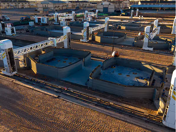 Gantry robotic 3D printers on rails printing concrete residential building shells in a production yard