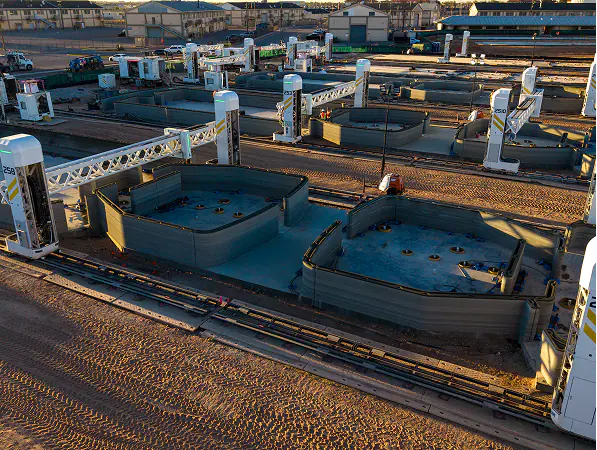 Gantry robotic 3D printers on rails printing concrete residential building shells in a production yard