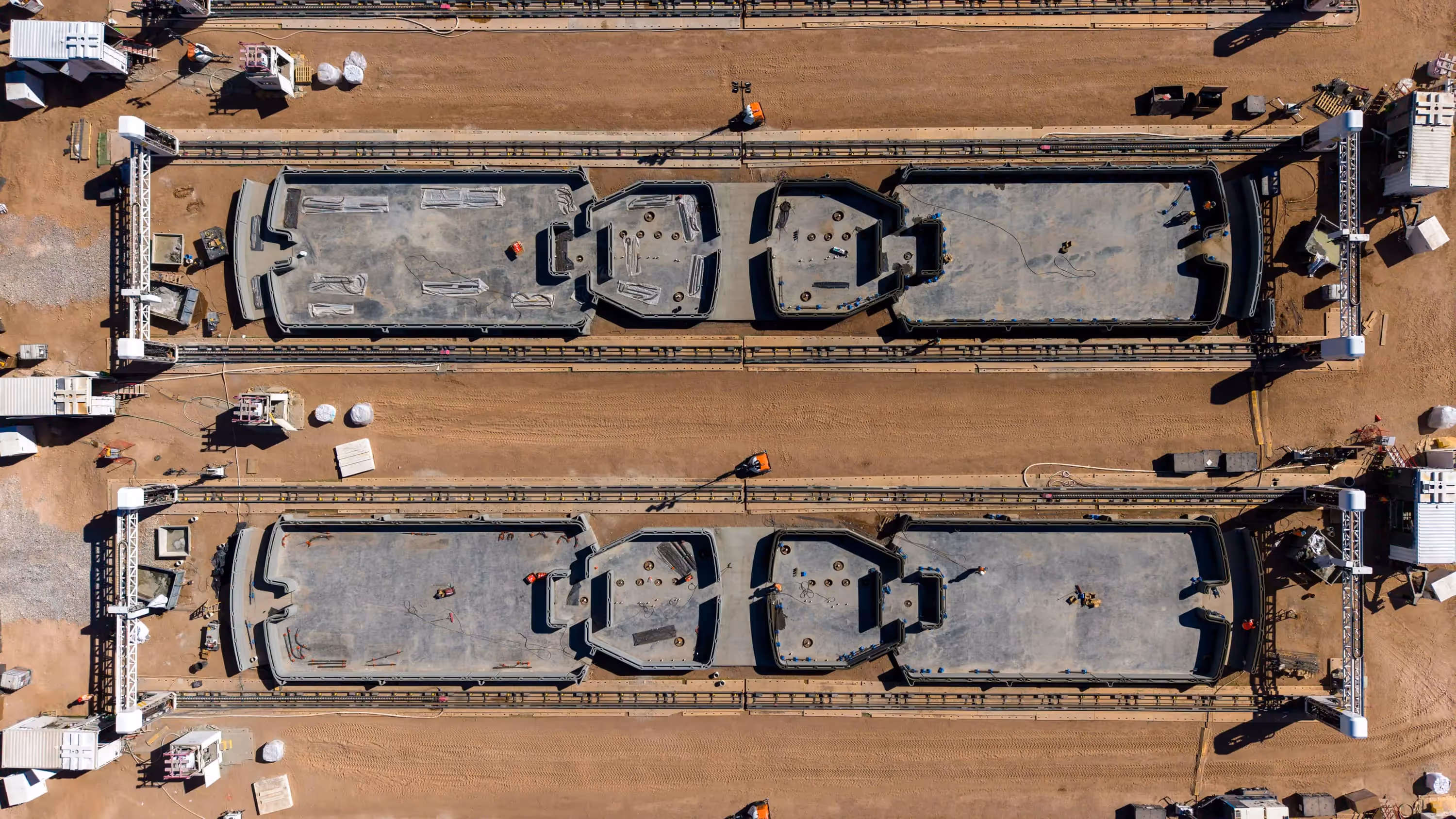 Aerial view of dual gantry robotic 3D printers printing modular concrete home foundations on a sandy construction site