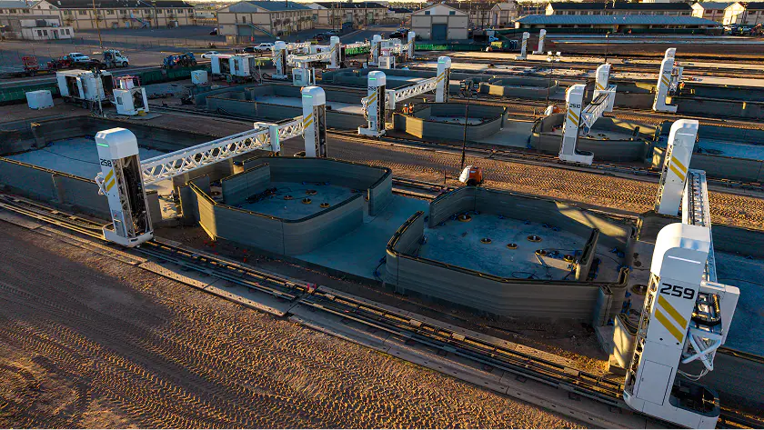 Gantry robotic 3D printers on rails printing concrete residential building shells in a production yard