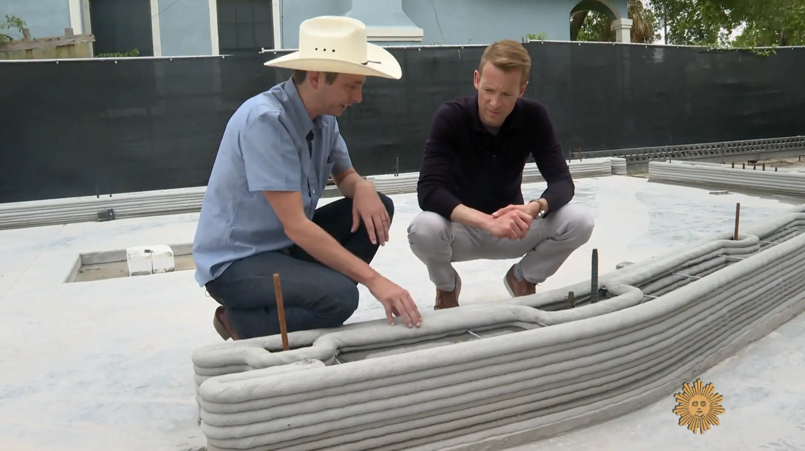 Two men inspecting layered 3D-printed concrete wall coils on a 3D-printed home foundation.