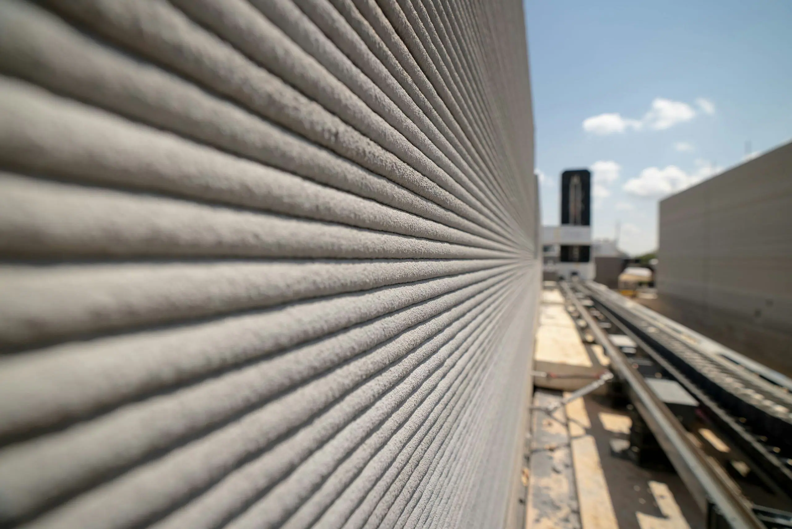 Layered 3D-printed concrete wall texture with robotic printing gantry and rails on construction site