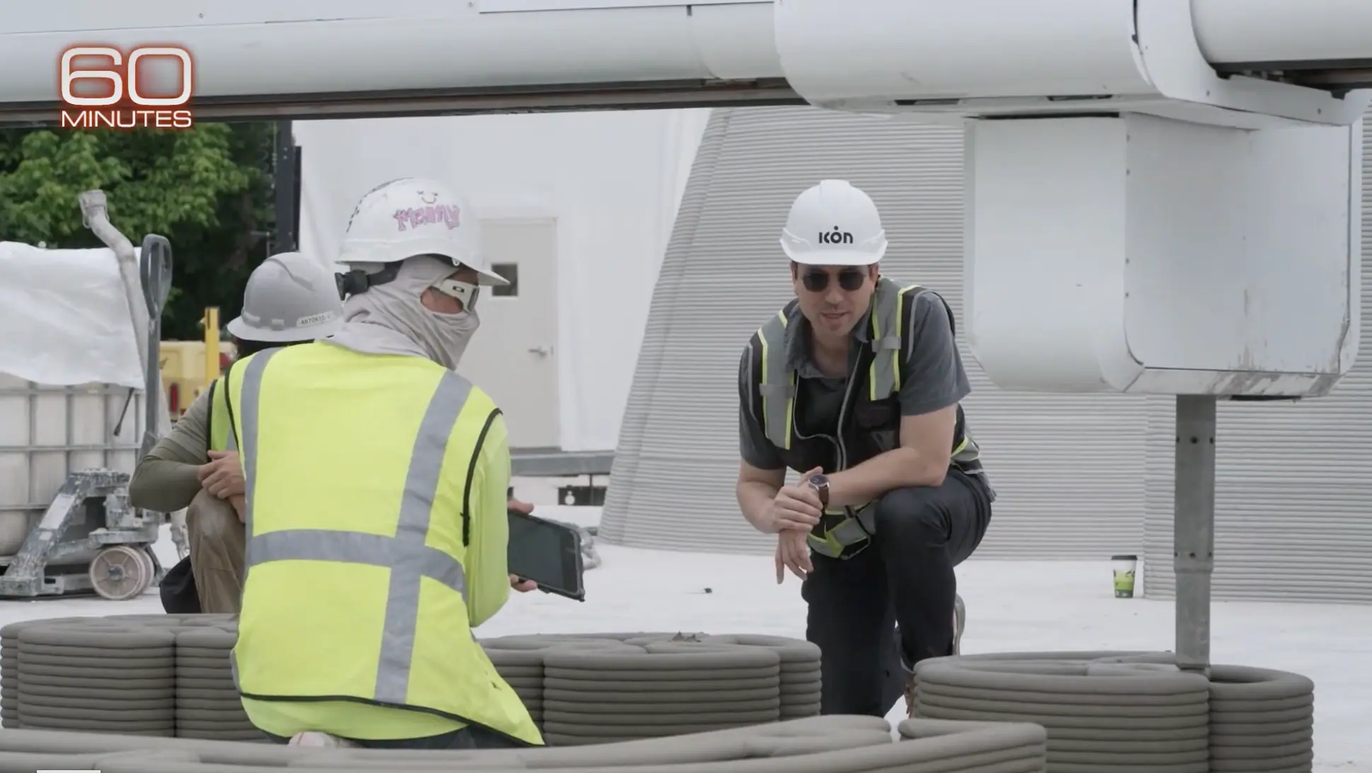 Worker in Icon hard hat and colleague reviewing tablet beside stacked 3D-printed concrete coils