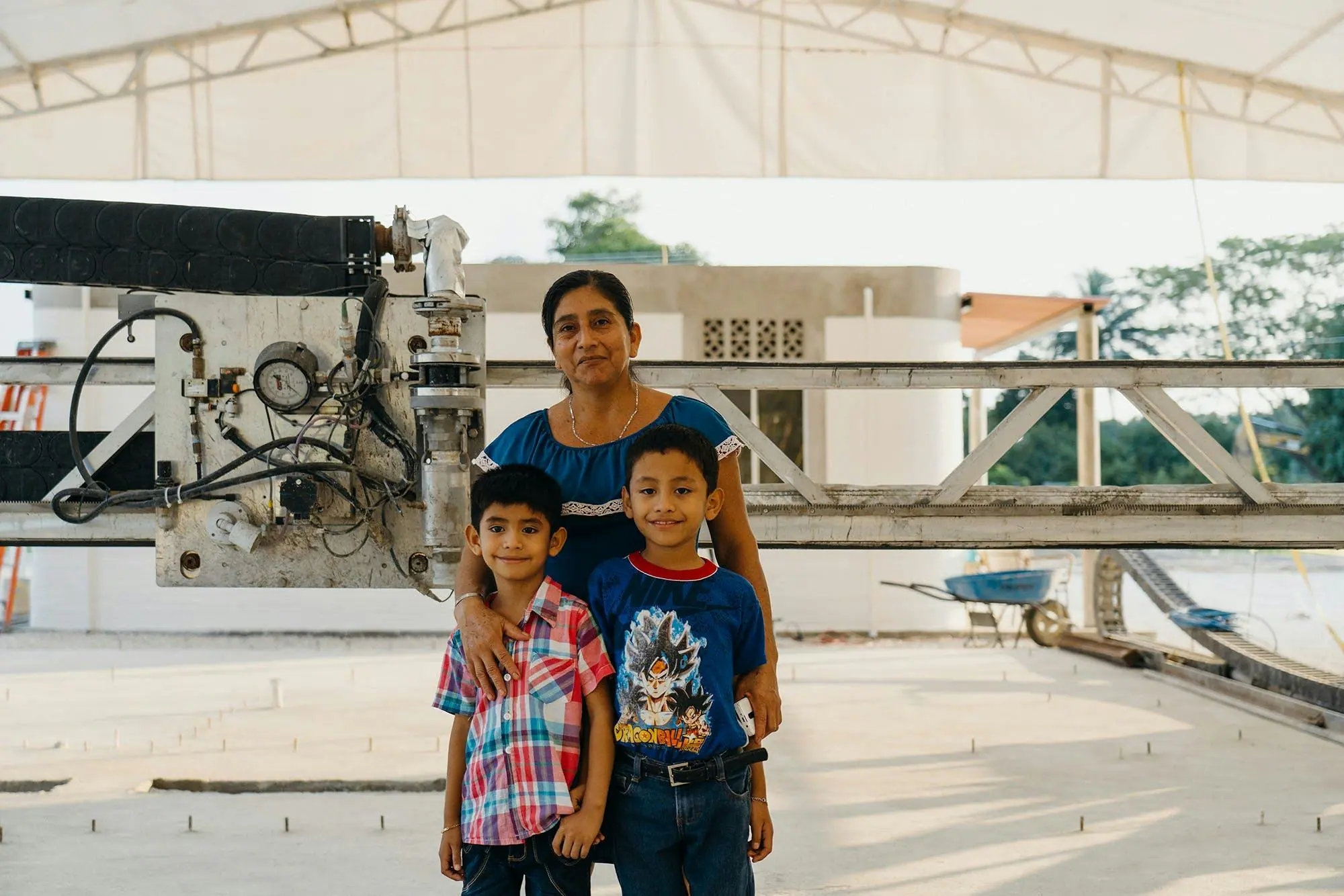 Family posing beside a robotic 3D‑printing concrete rig at a community housing construction site