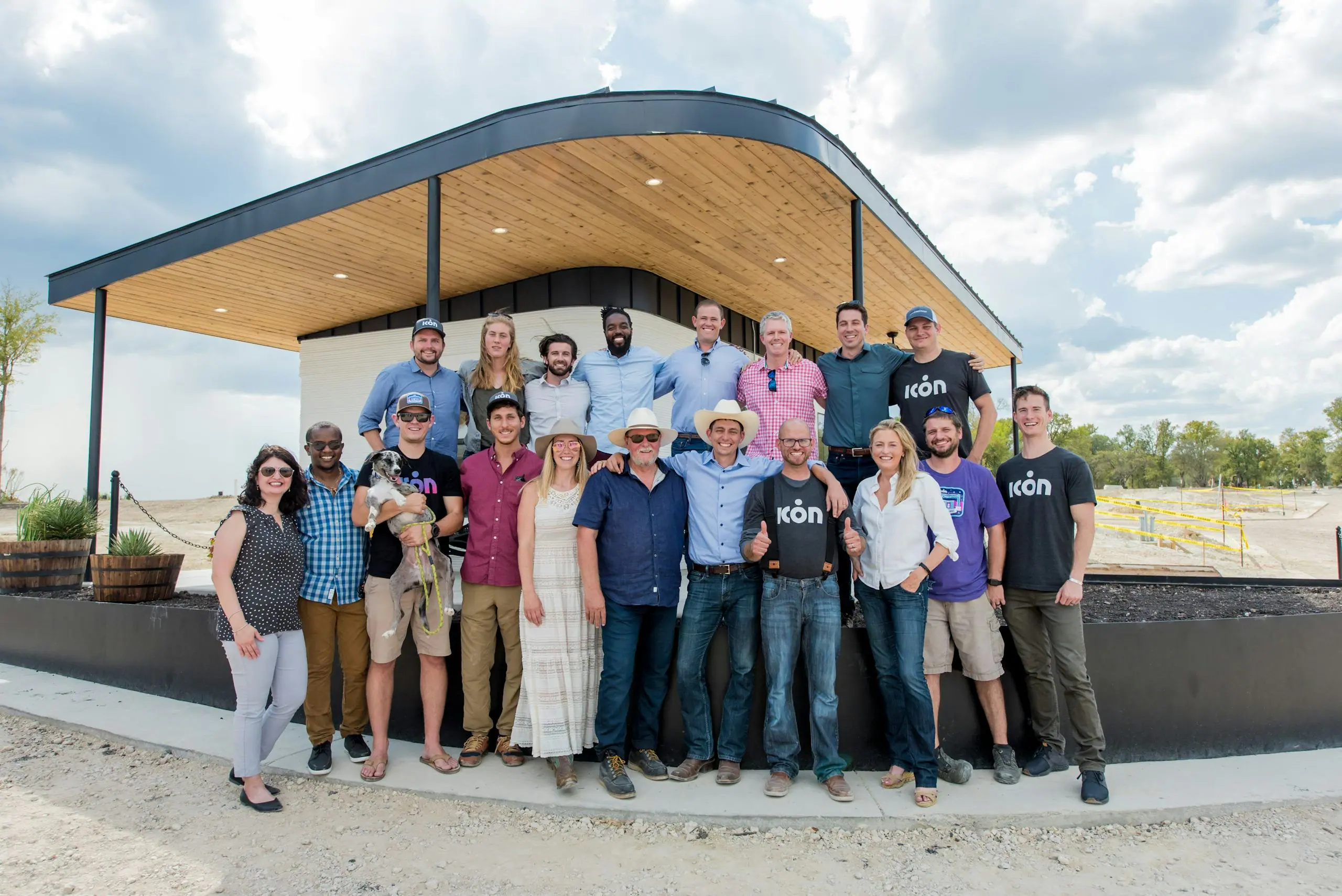 Icon Build team posing under curved wood canopy at completed 3D-printed home site