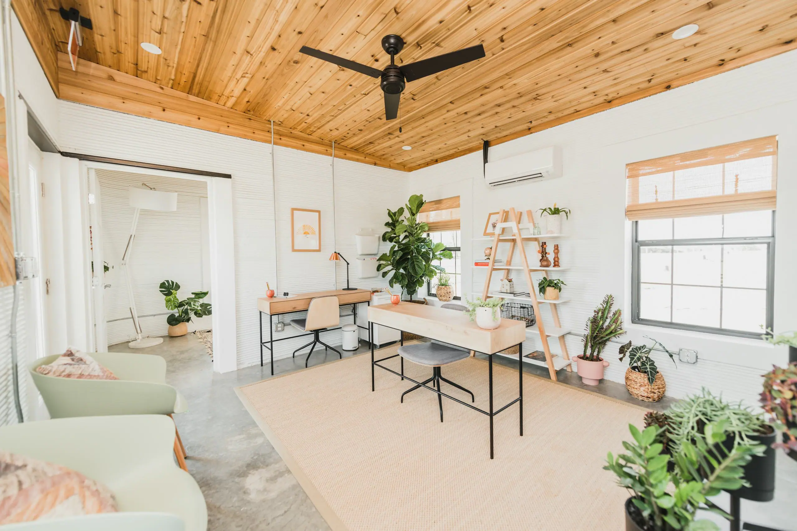 Bright design-build workspace showcasing wood-plank ceiling, textured white walls, desks and indoor plants