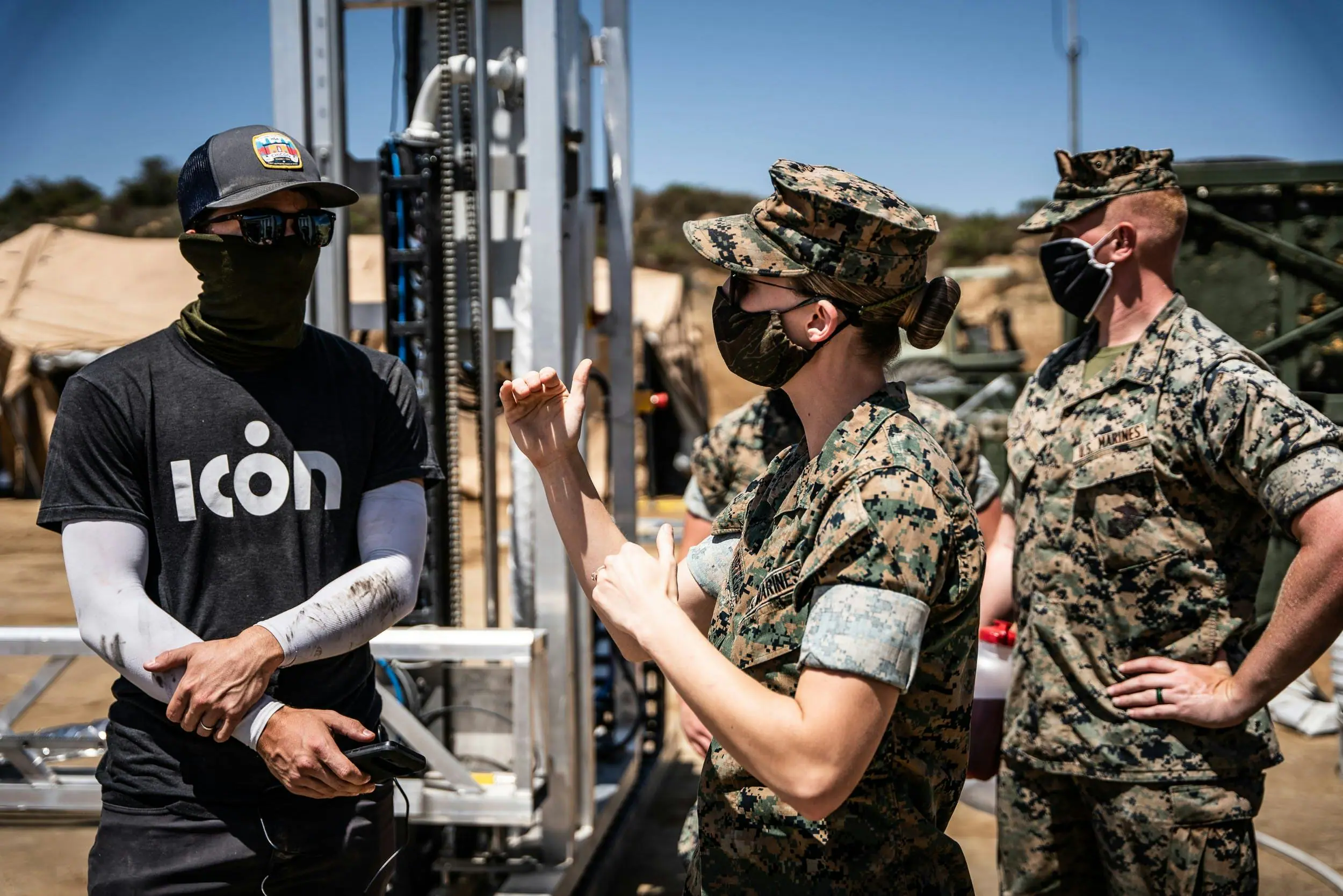 Icon Build technician consulting with U.S. Marines beside robotic 3D-printing construction equipment on site