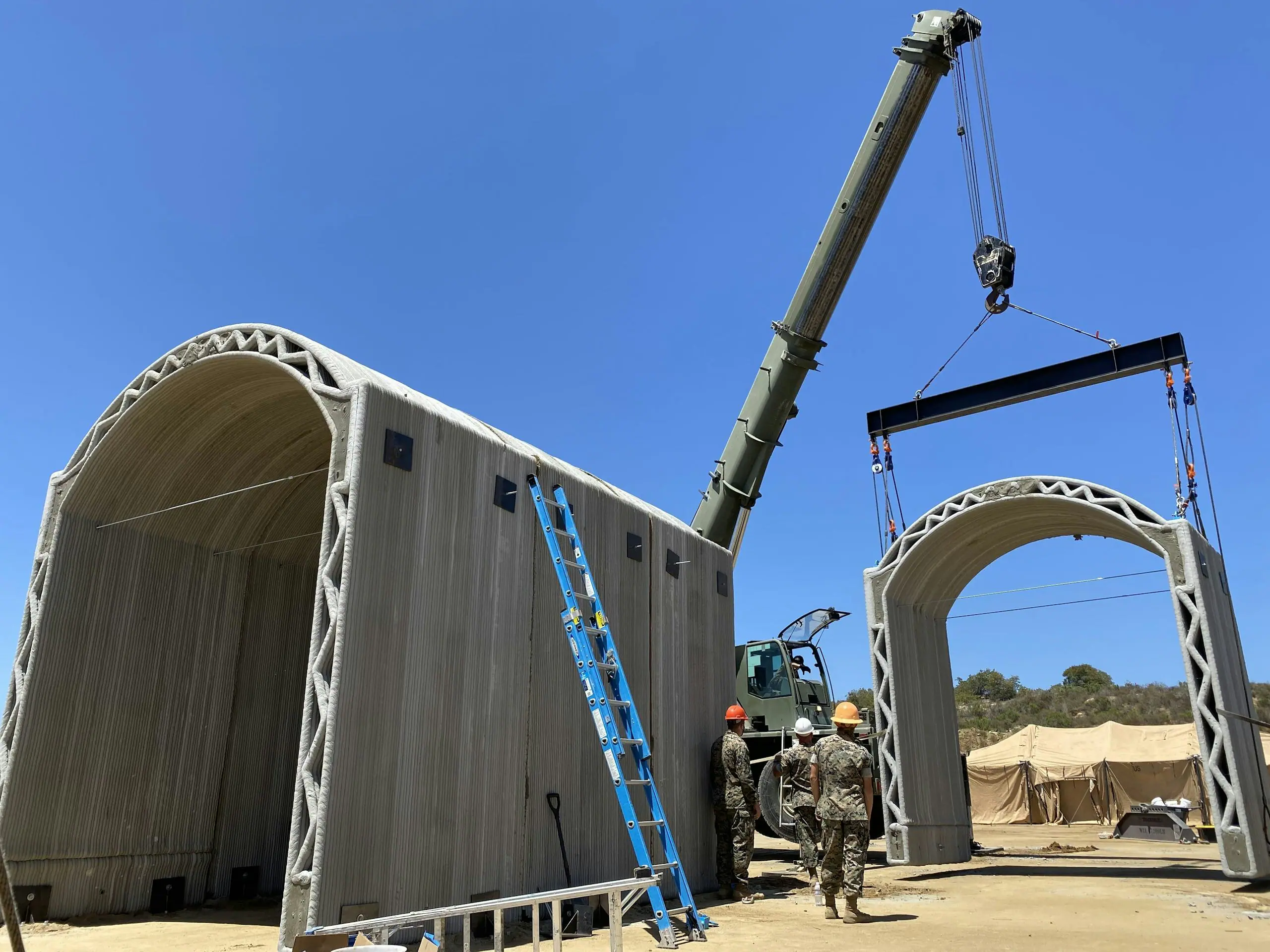 Crane lifting 3D-printed concrete arch module while crew guide assembly at a modular construction site