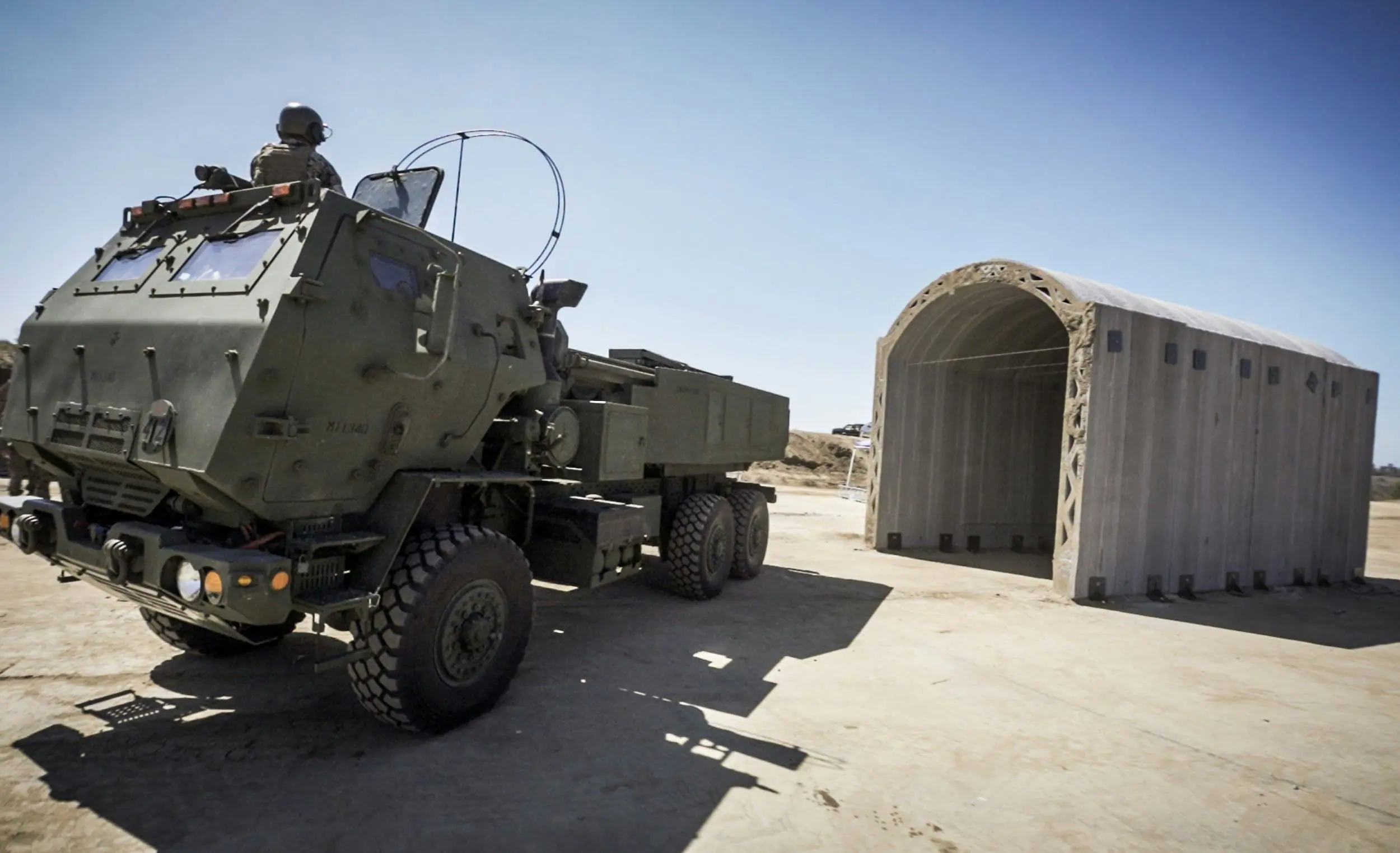 Armored military truck beside a 3D-printed concrete arch shelter illustrating rapid-deploy modular housing