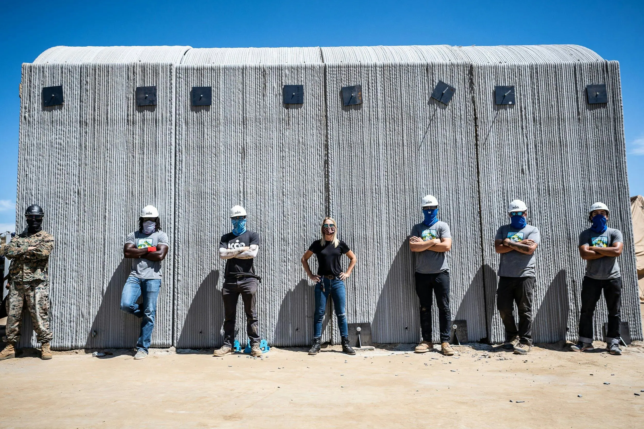 Construction team in hard hats standing before large 3D-printed concrete wall panels showcasing layered print texture