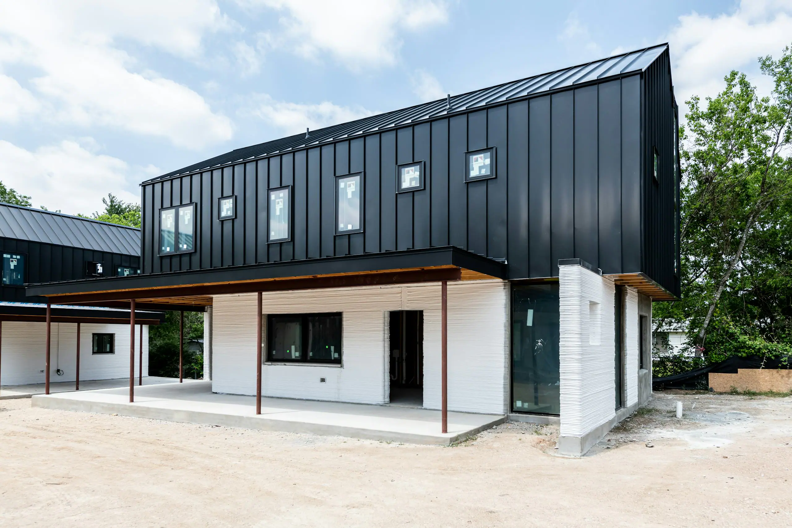 Black metal-clad upper volume and 3D-printed white lower walls of a modern home under construction