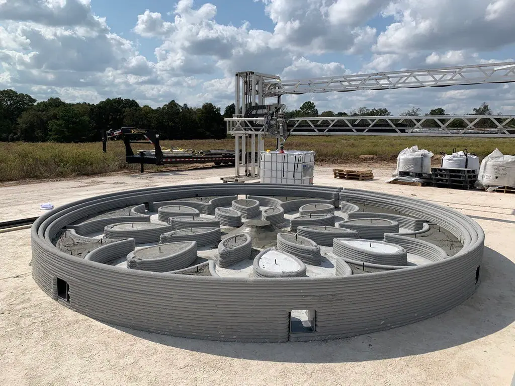 Circular 3D‑printed concrete foundation with internal partition walls, printed by gantry robotic printer on a construction site