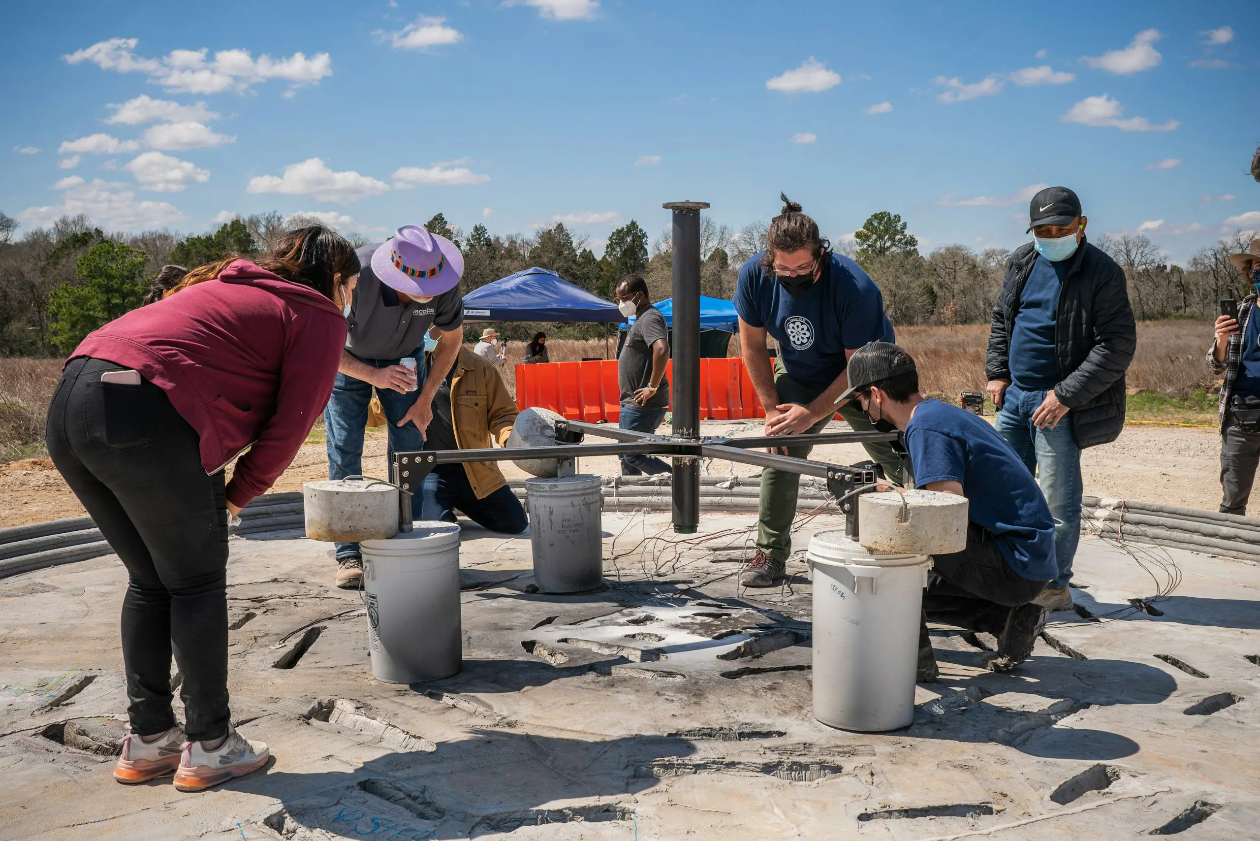 Engineers and community members inspect 3D-printing gantry and fresh printed concrete foundation on site