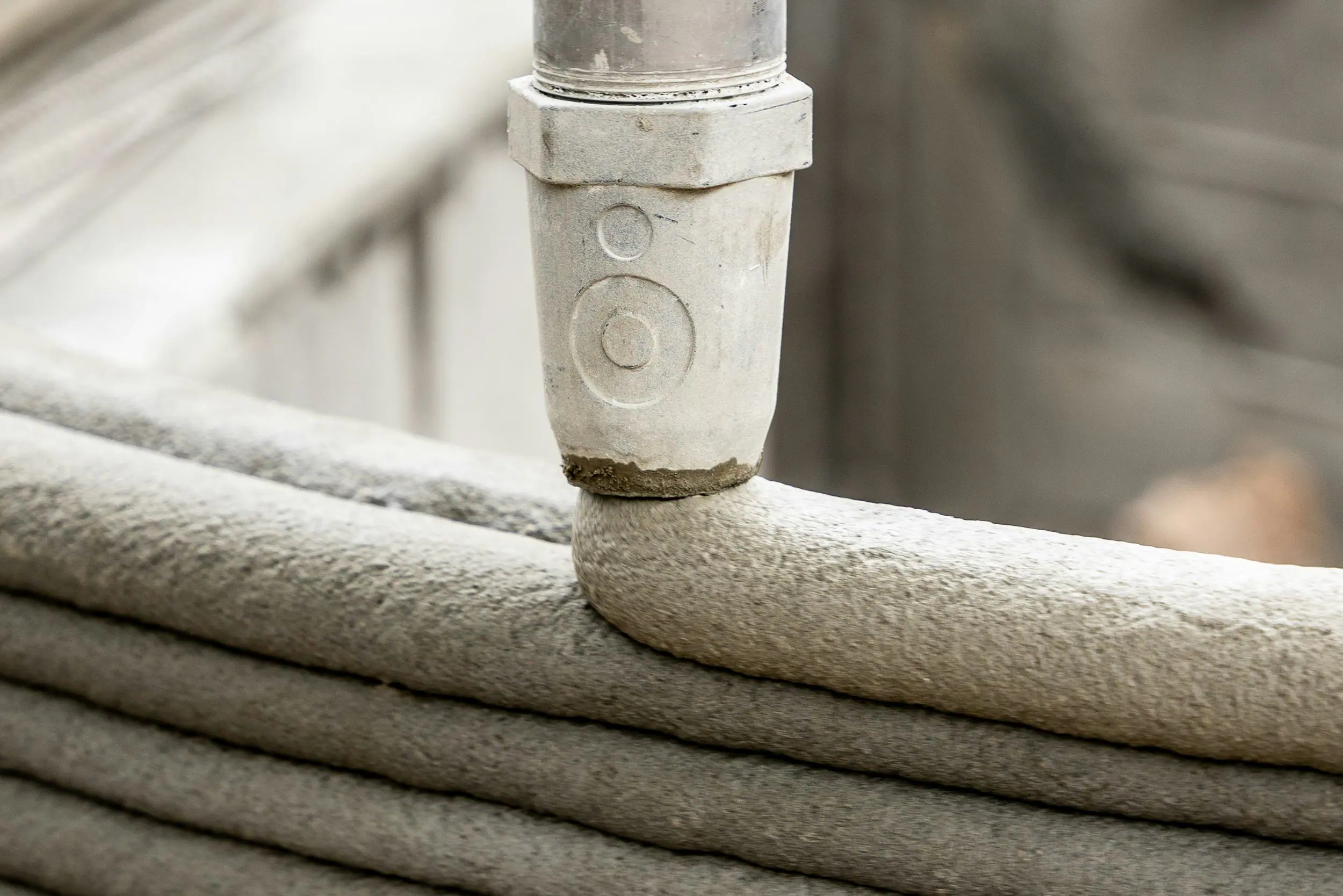 Robotic extrusion nozzle depositing layered concrete for 3D-printed wall construction