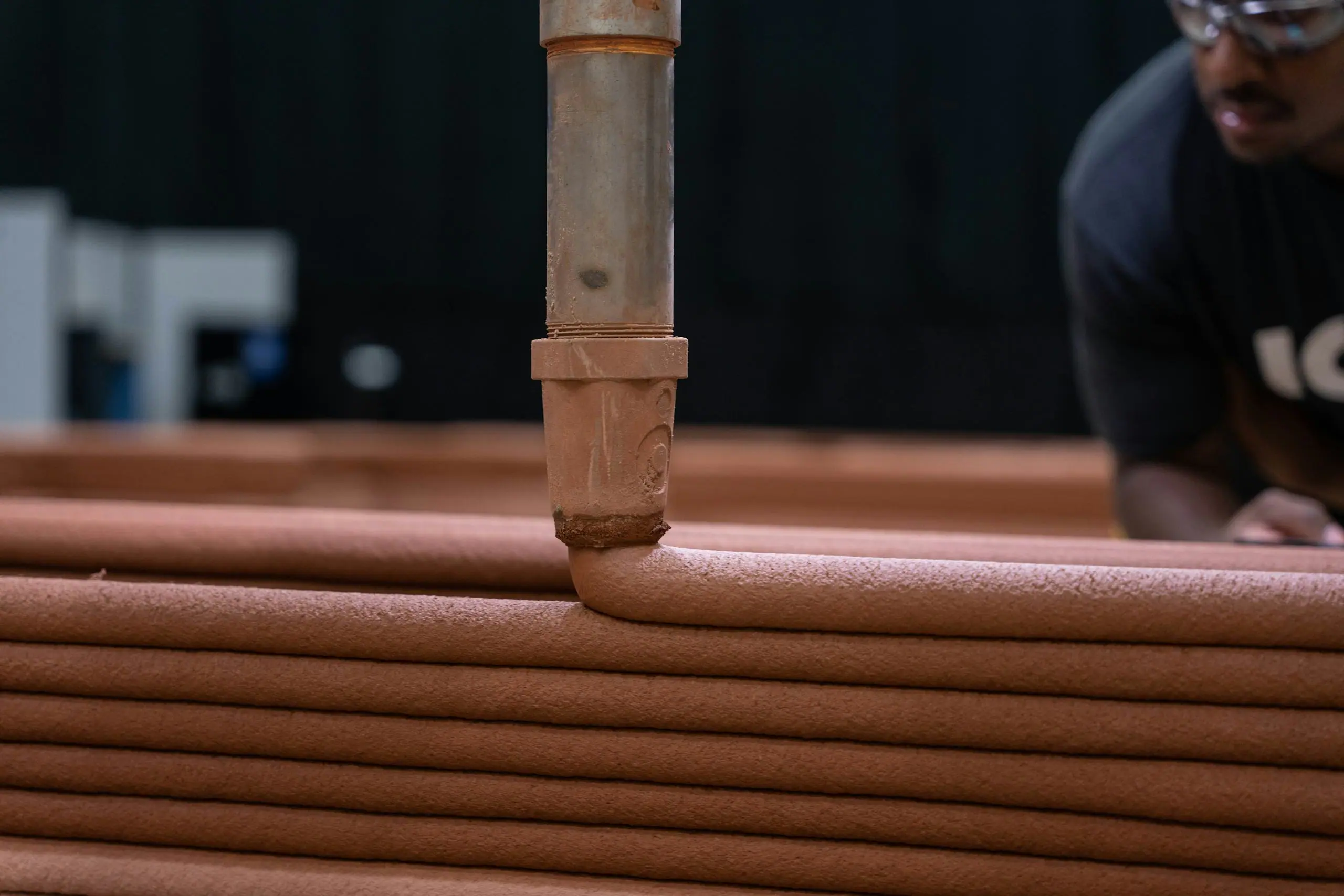 Robotic extrusion nozzle laying successive coils of 3D-printed concrete to form layered wall sections