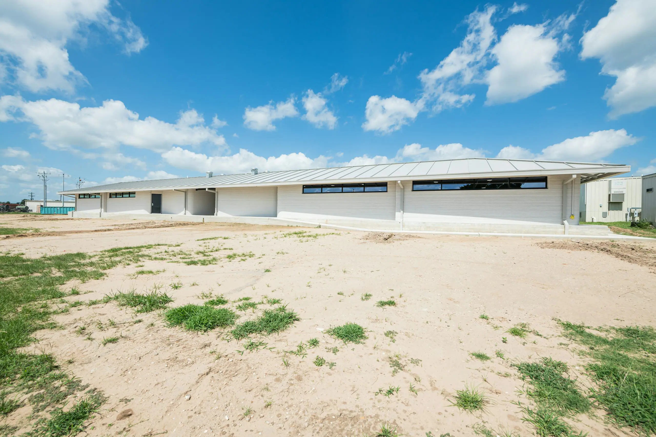 Low-profile single-story building with metal roof and horizontal clerestory windows on a cleared construction site