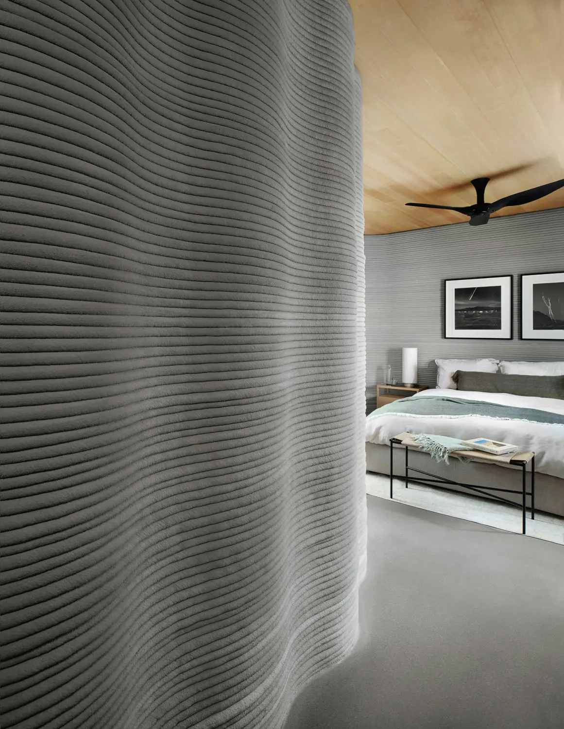 Curved ribbed 3D-printed interior wall with visible layer lines opening into a modern bedroom with wood ceiling