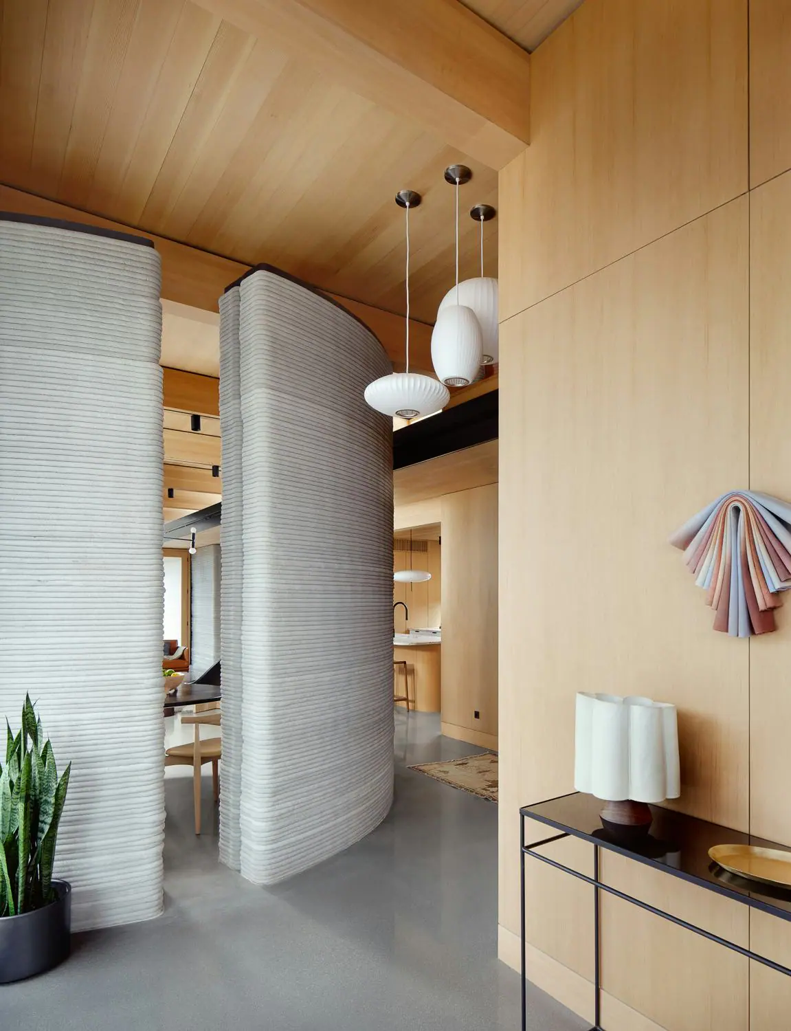 Curved ribbed 3D-printed room partitions separating a dining area in a warm timber-paneled interior