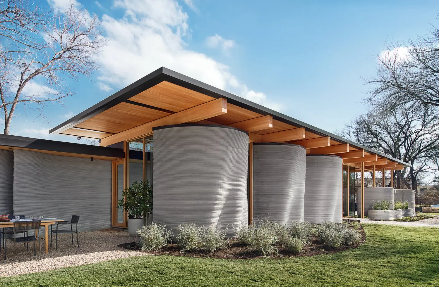 Modern home with curved 3D-printed concrete walls and wide timber overhang, illustrating robotic construction and design-build