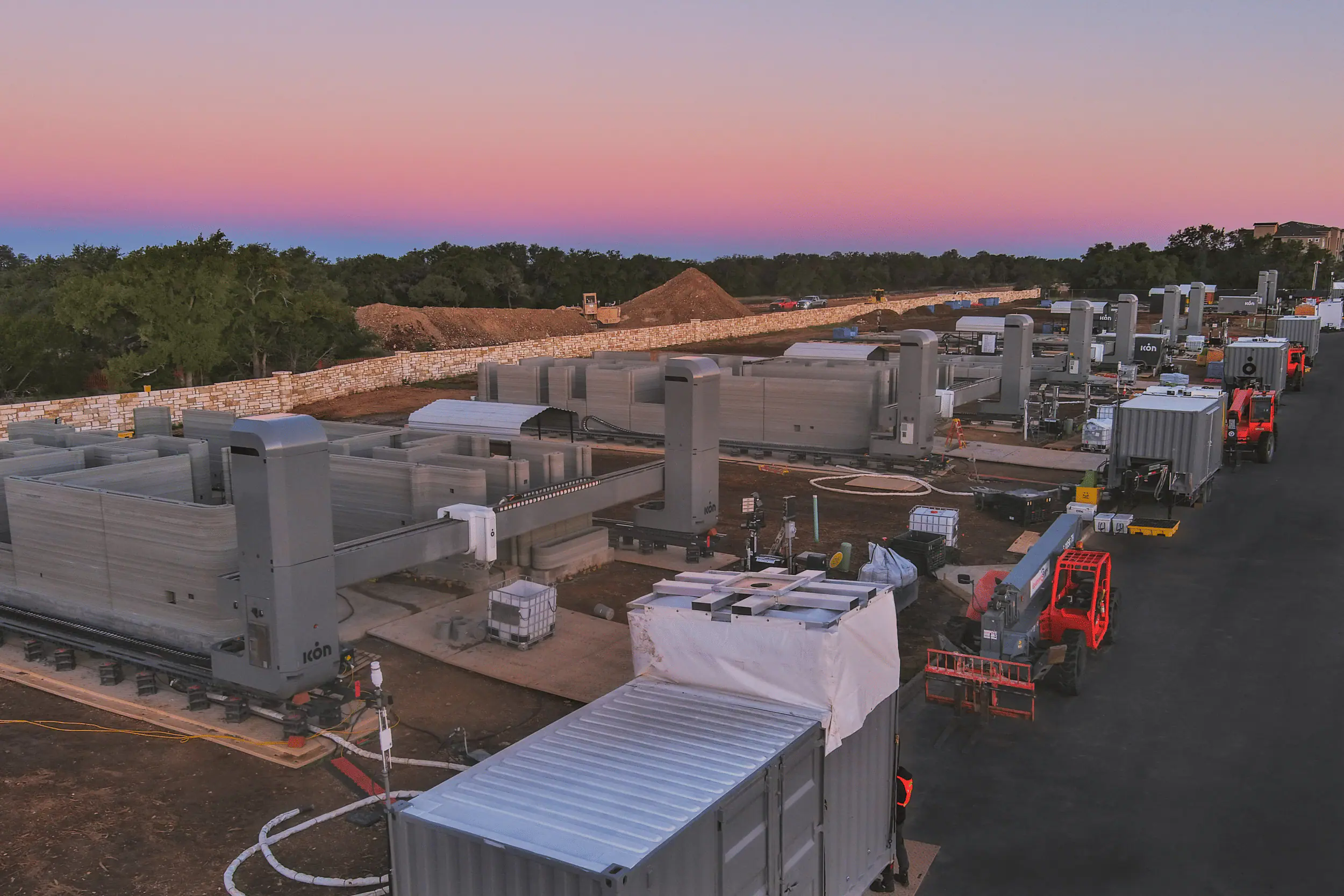 Robotic 3D-printing gantries forming concrete wall panels across a residential construction site at dusk
