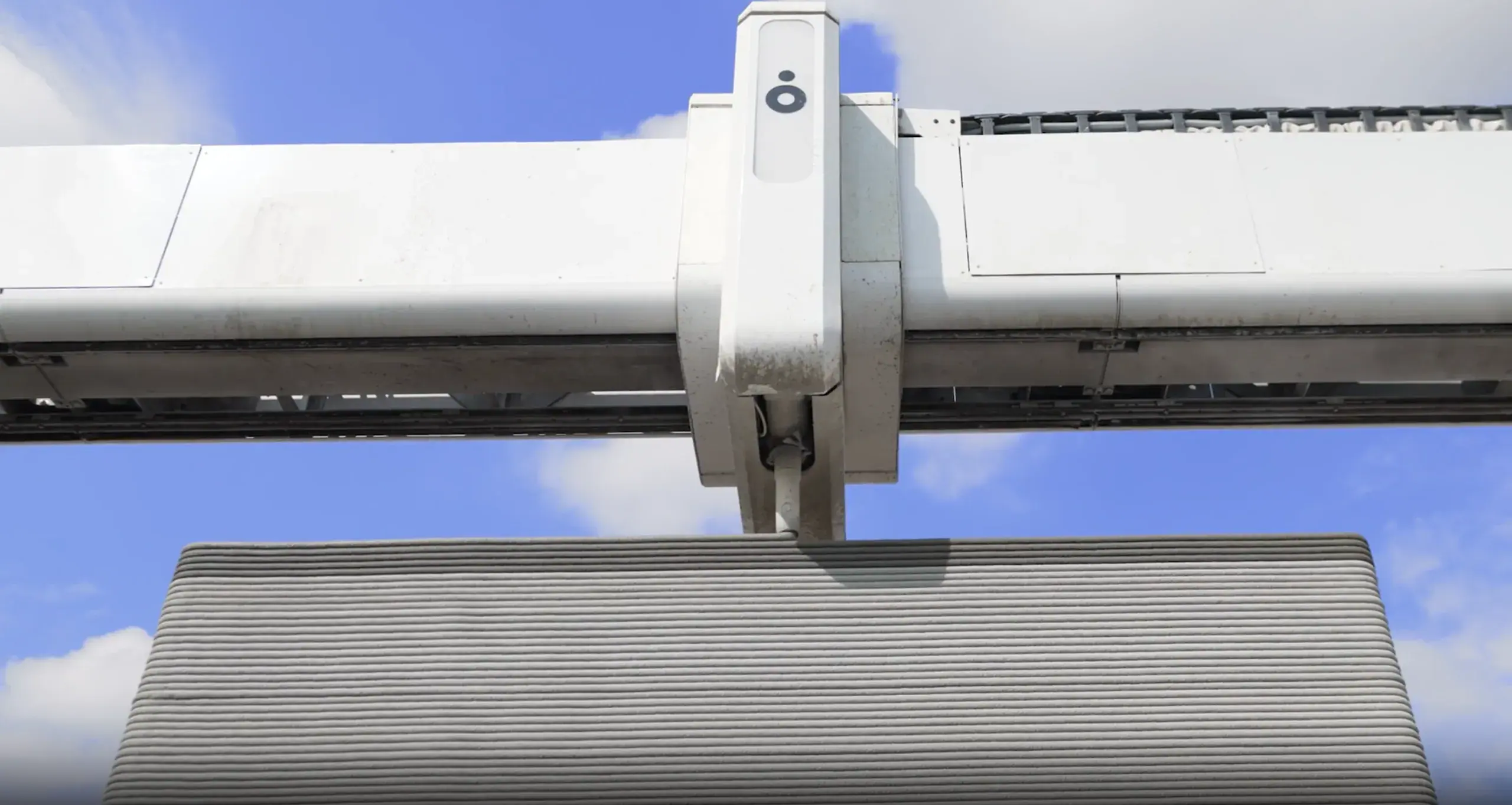 Gantry-mounted robotic 3D-printing head extruding layered ribbed concrete wall panels under a track system