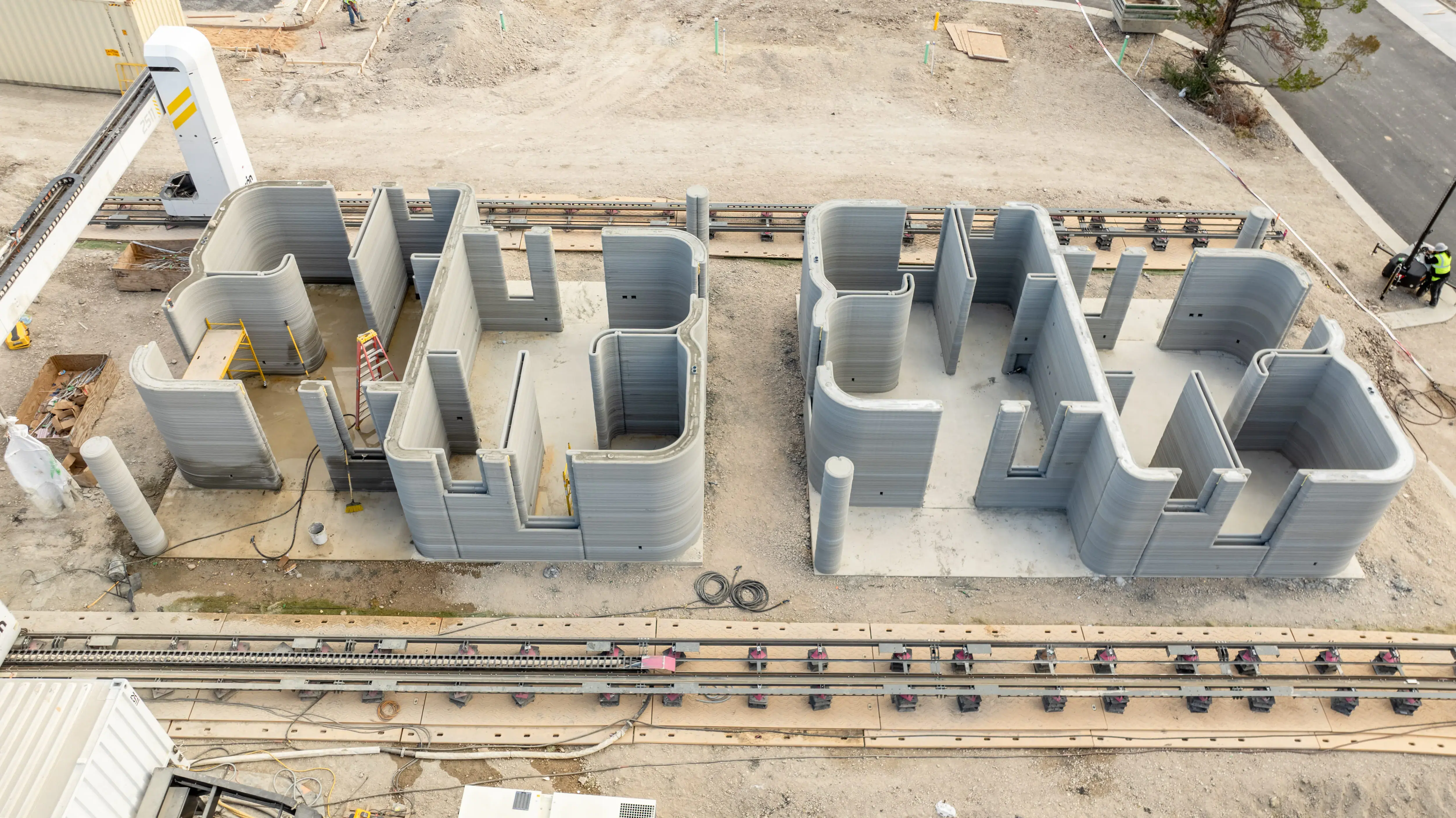 Gantry 3D printer producing concrete home shells with layered walls, illustrating robotic 3D-printed construction.