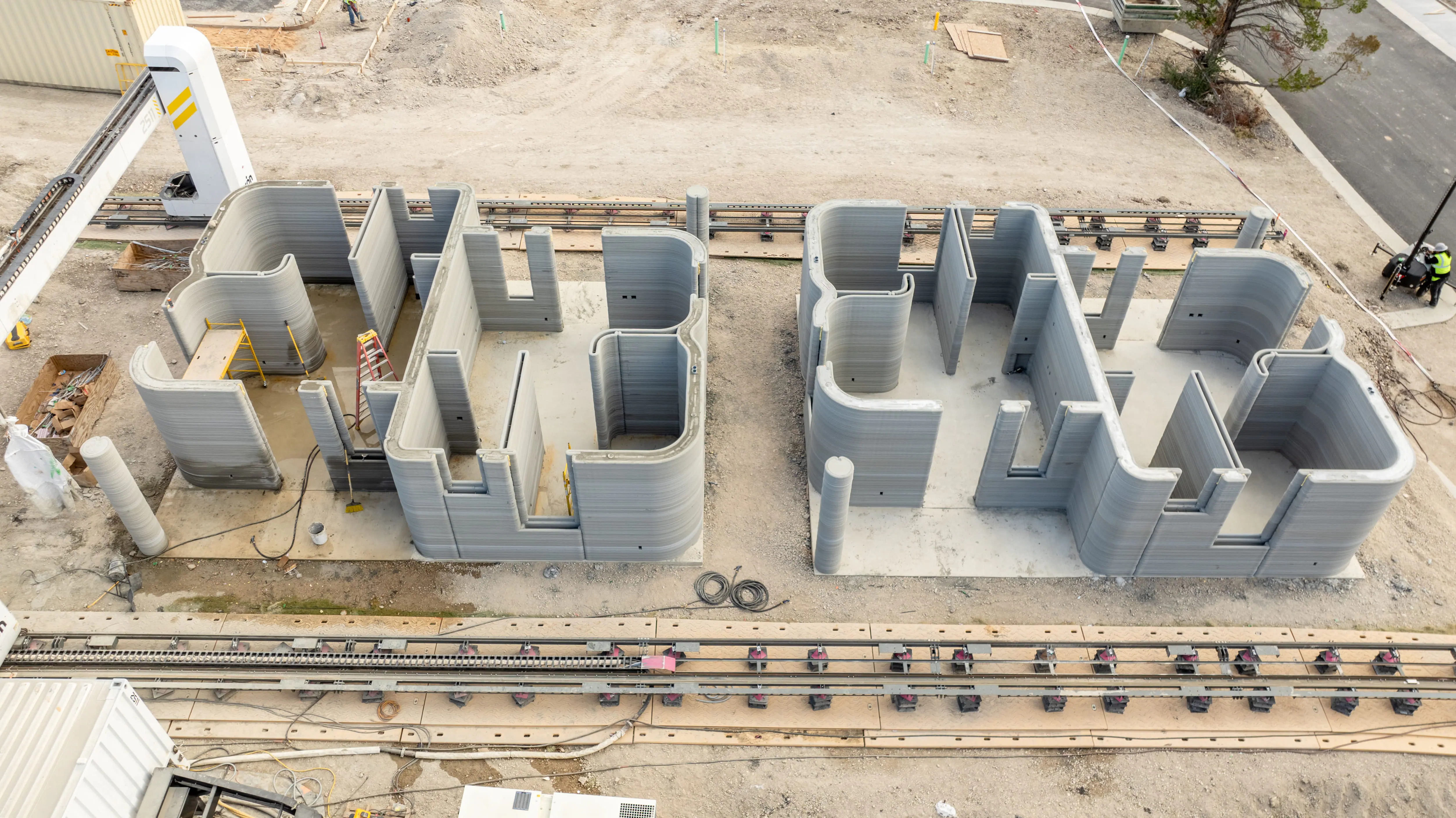 Gantry 3D printer producing concrete home shells with layered walls, illustrating robotic 3D-printed construction.