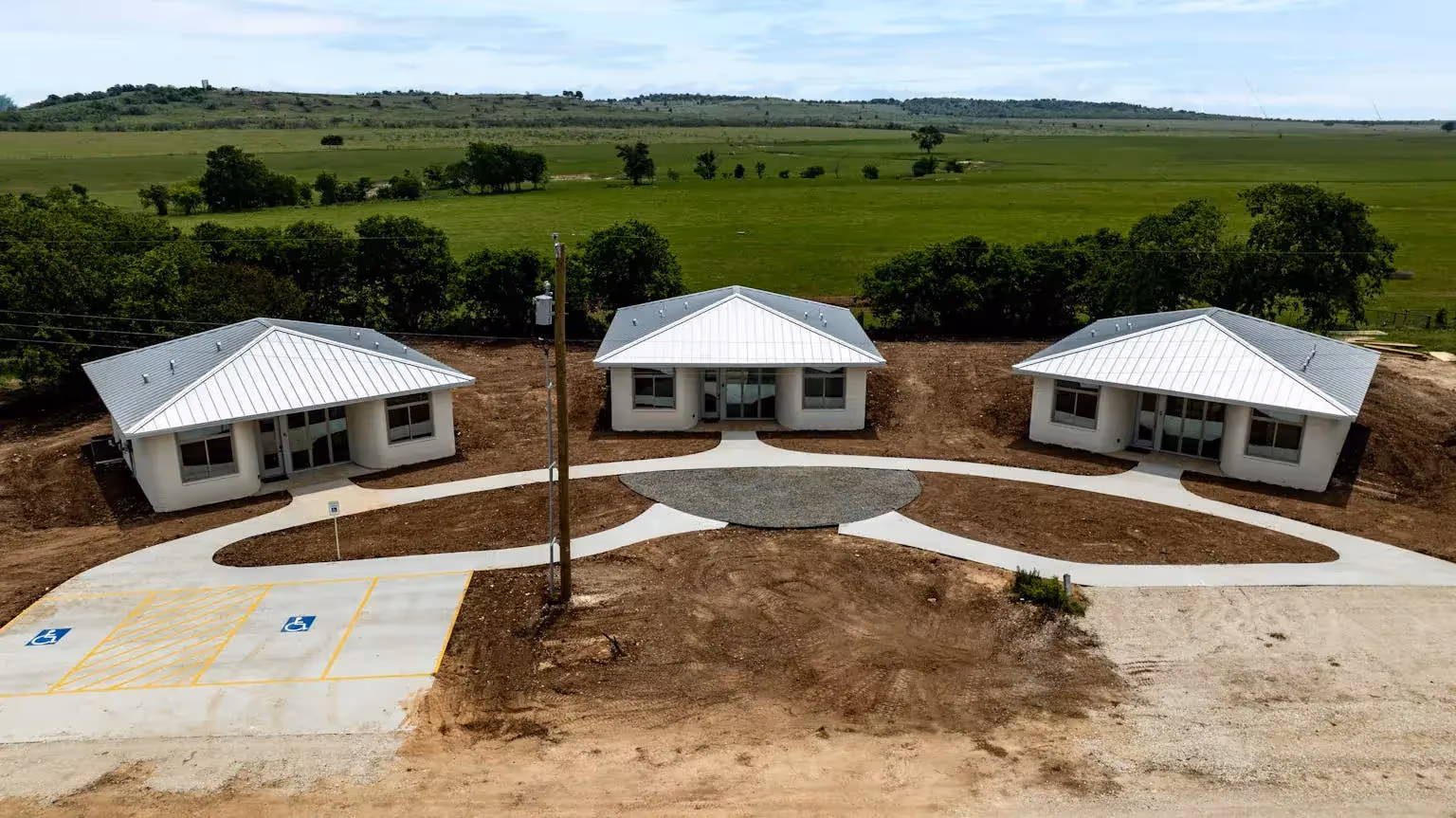 Three single-story concrete homes with metal roofs and shared circular walkway, showcasing rapid 3D-printed community housing.