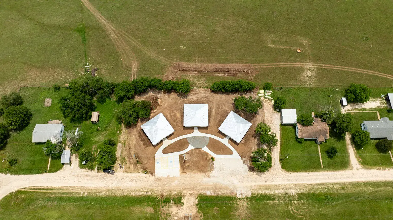 Aerial view of three small homes clustered around a shared circular courtyard on a rural design-build construction site