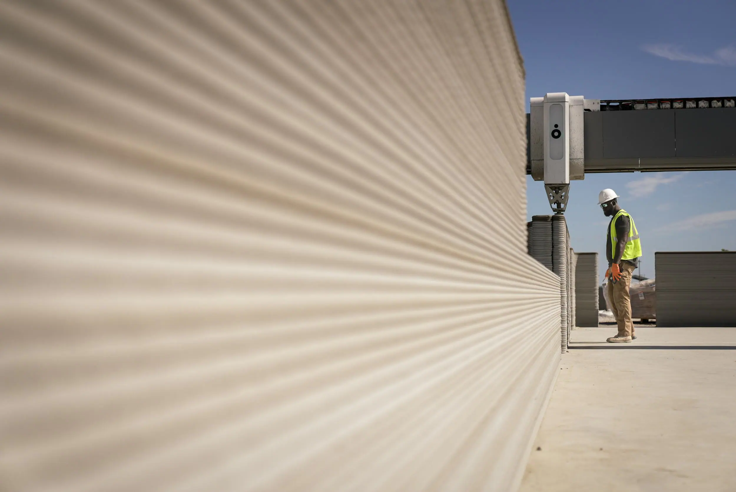 Textured 3D-printed concrete wall with gantry printer and worker in hard hat inspecting printed layers