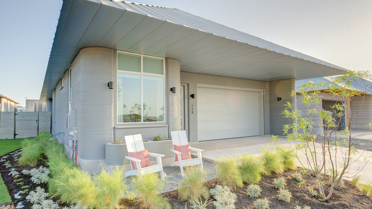 Modern home exterior with 3D-printed textured walls, two white chairs and garage door