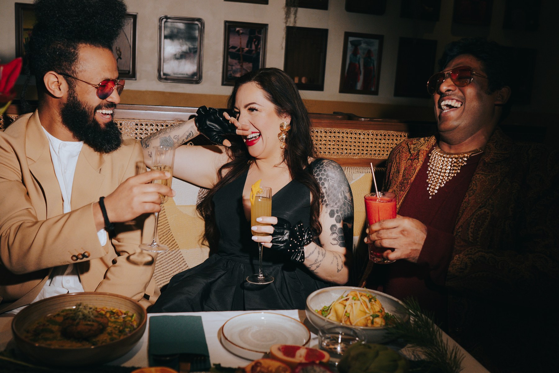 Friends laughing and toasting with cocktails over shared Indian dishes at Miri Mary Amsterdam before a night out.