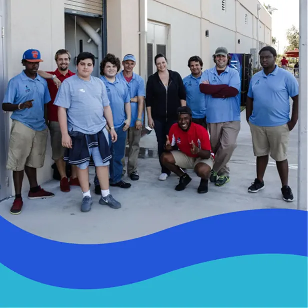 Group of diverse people smiling and posing outside a building, some wearing light blue shirts and casual clothing.